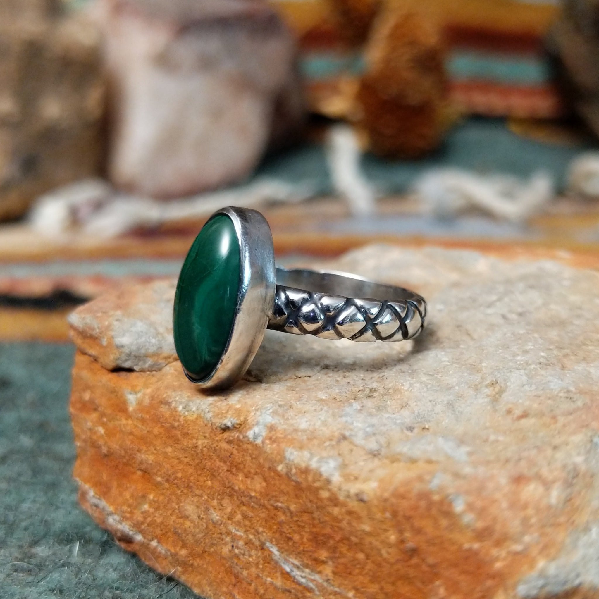 Raymond Coriz sterling silver ring featuring an elongated oval green malachite cabochon with natural dark banding and a textured knurled silver band; side view.
