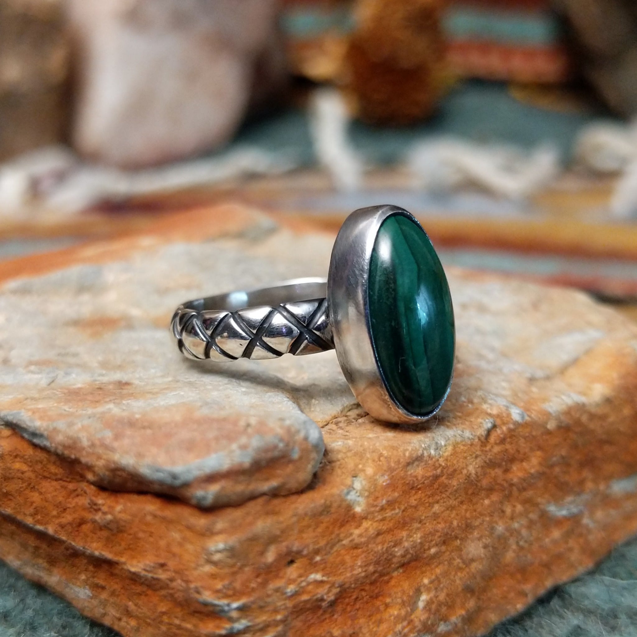 Raymond Coriz sterling silver ring featuring an elongated oval green malachite cabochon with natural dark banding and a textured knurled silver band; side view.