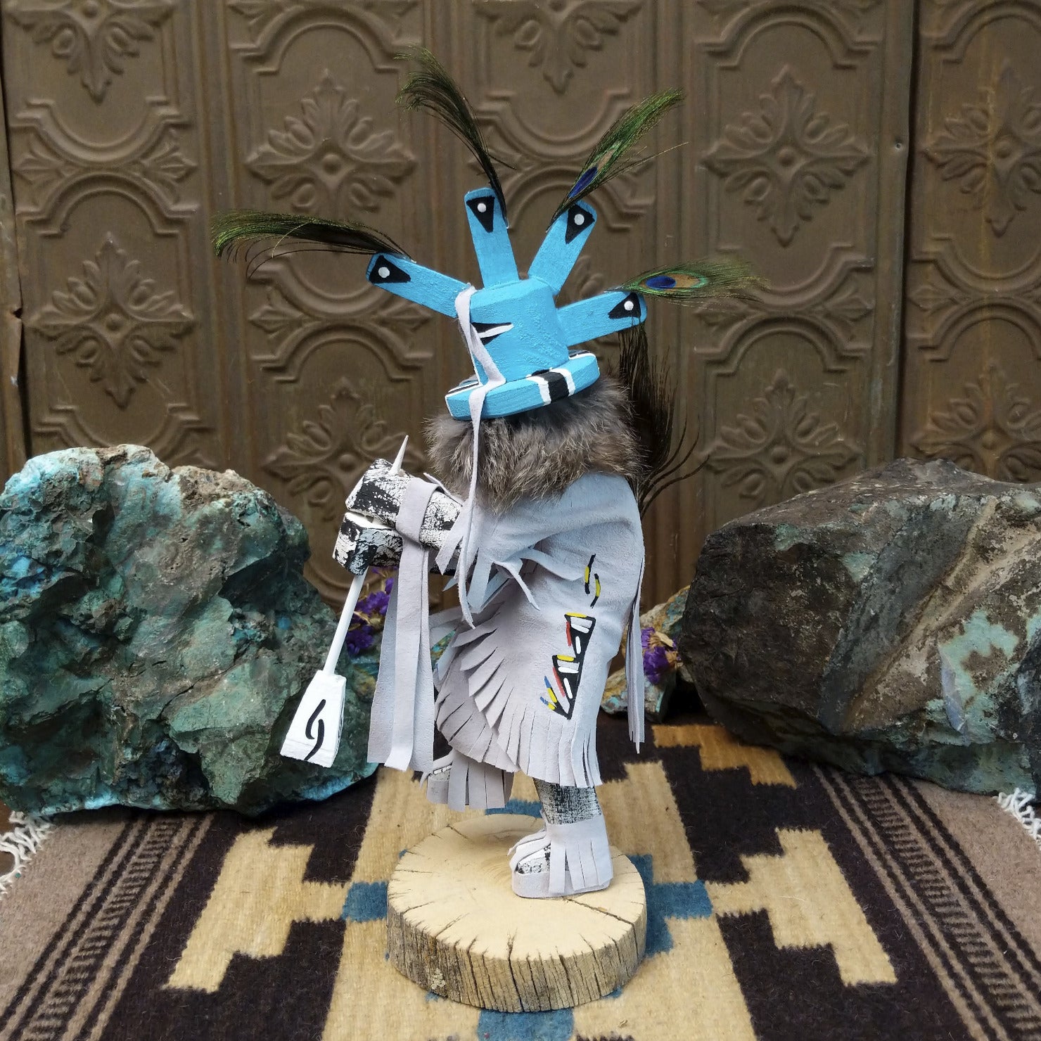 Navajo-made Kokopelli kachina doll by M. C. with blue headdress, peacock feathers, flute, and gray garments.