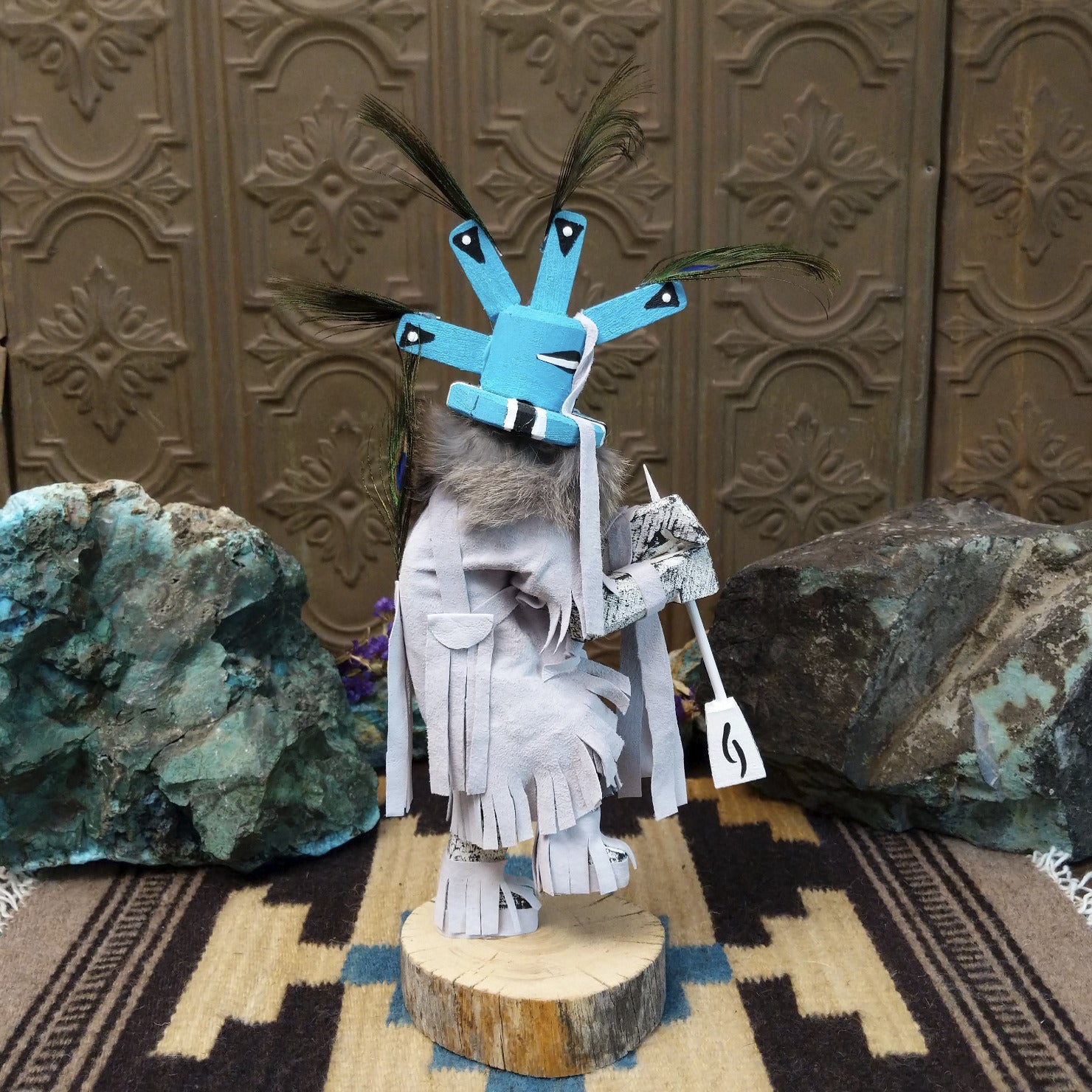 Navajo-made Kokopelli kachina doll by M. C. with blue headdress, peacock feathers, flute, and gray garments.