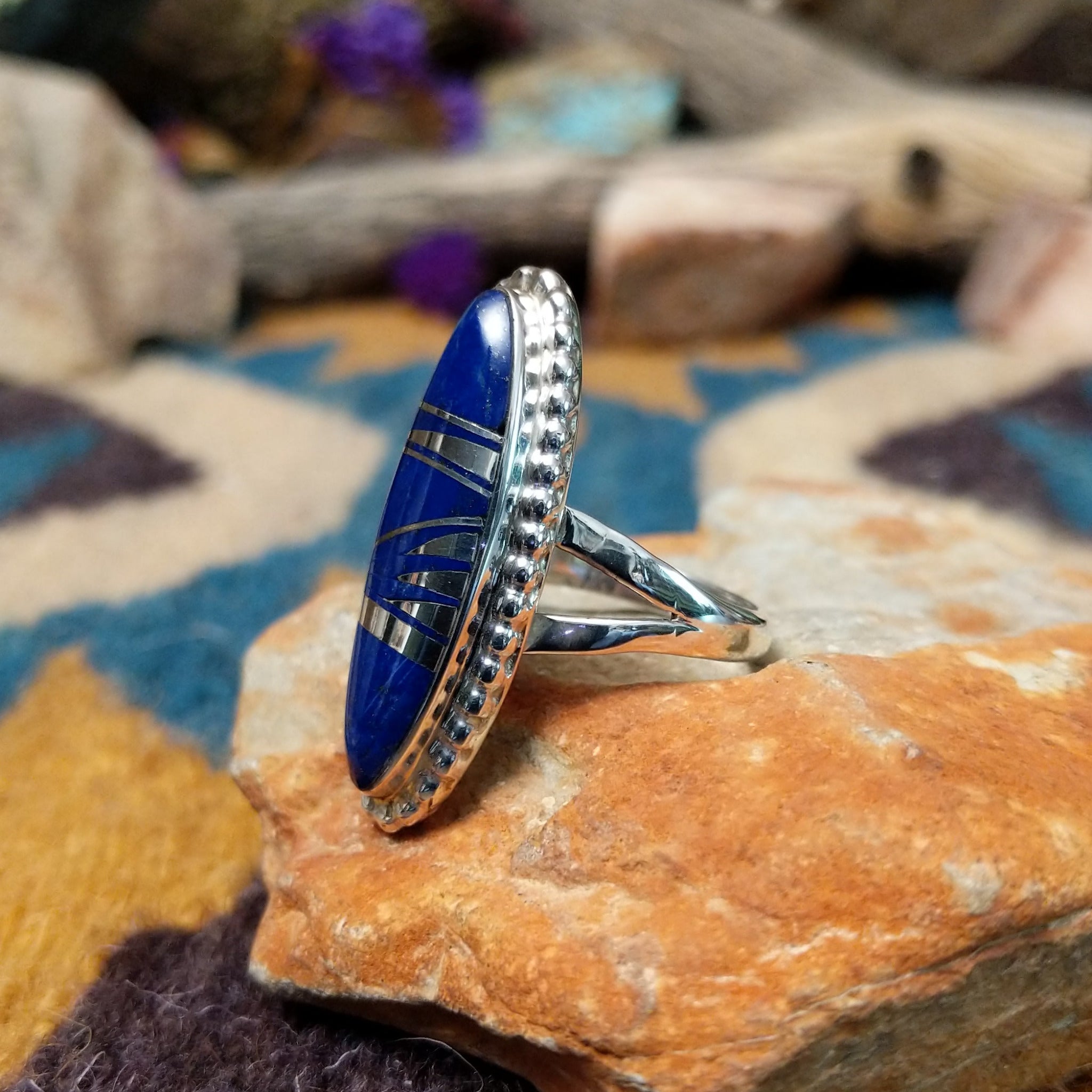 Handcrafted sterling silver ring featuring an elongated marquise-shaped lapis lazuli inlay with diagonal sterling silver geometric accents, framed by a beaded silver border and set on a split sterling silver band; side view.