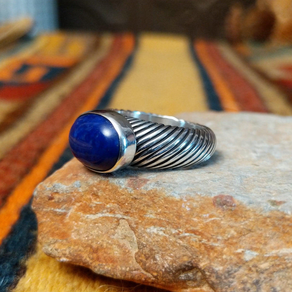 Angled side view of a lapis lazuli ring showing the raised oval stone setting and deeply grooved, rope-like silver band.