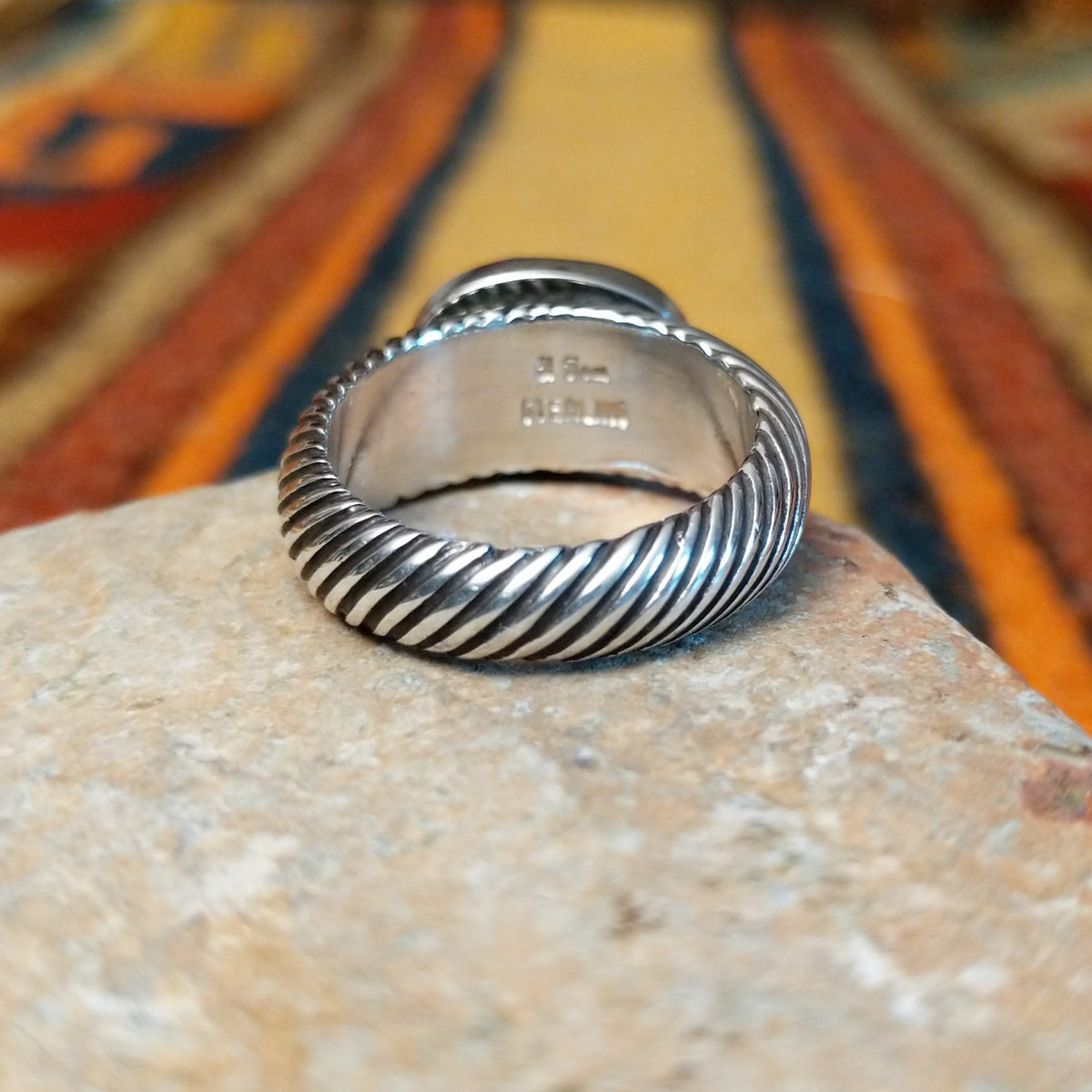 Close-up of the interior of a silver lapis lazuli ring showing the artist's stamped signature and STERLING hallmark, with diagonal ribbed detailing along the band.