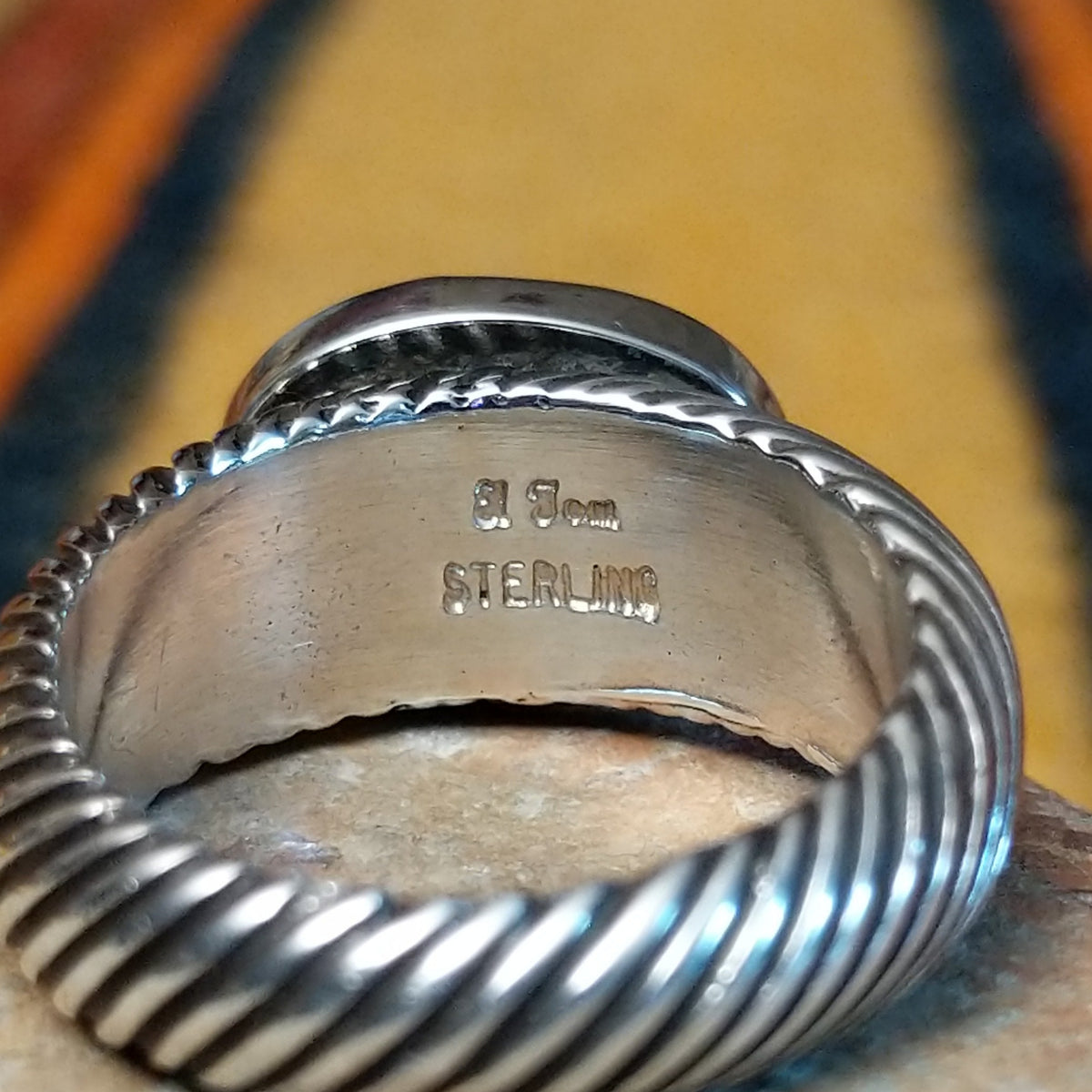 Close-up of the interior of a silver lapis lazuli ring showing the artist's stamped signature and STERLING hallmark, with diagonal ribbed detailing along the band.