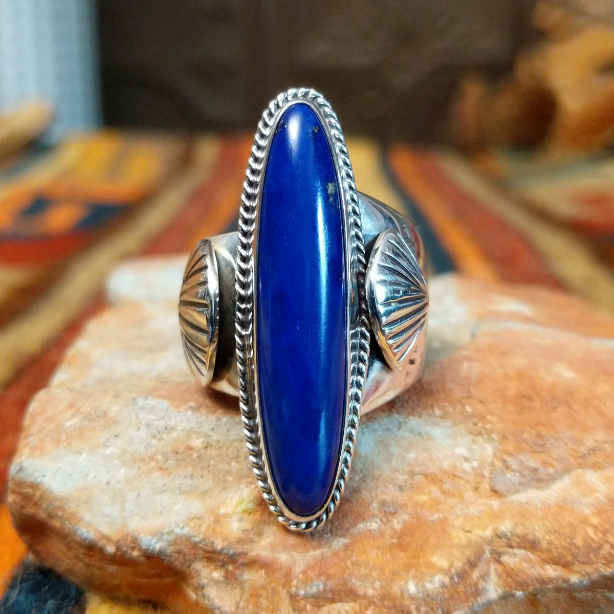 Lapis Ring by J. Chee featuring an elongated oval royal blue lapis lazuli stone set in sterling silver with a twisted rope bezel and decorative scalloped side accents.