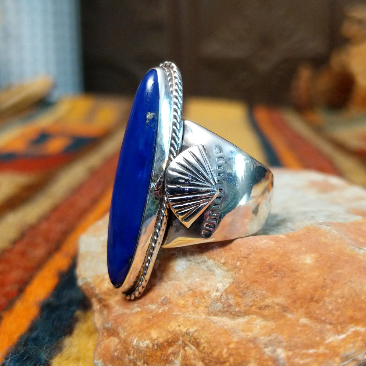 Lapis Ring by J. Chee featuring an elongated oval royal blue lapis lazuli stone set in sterling silver with a twisted rope bezel and decorative scalloped side accents; side view.