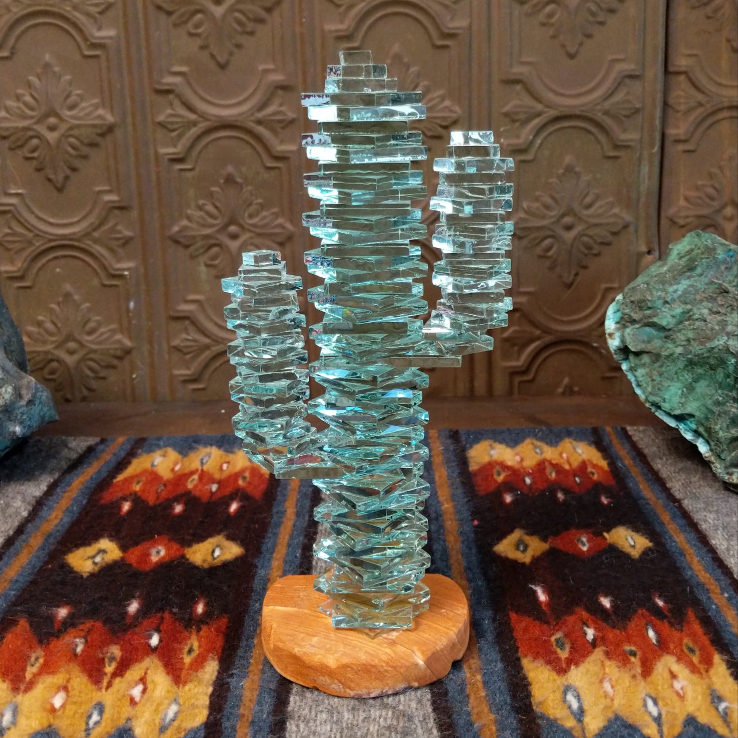 A glass cactus sculpture with translucent aqua glass mounted on a smooth sandstone base.