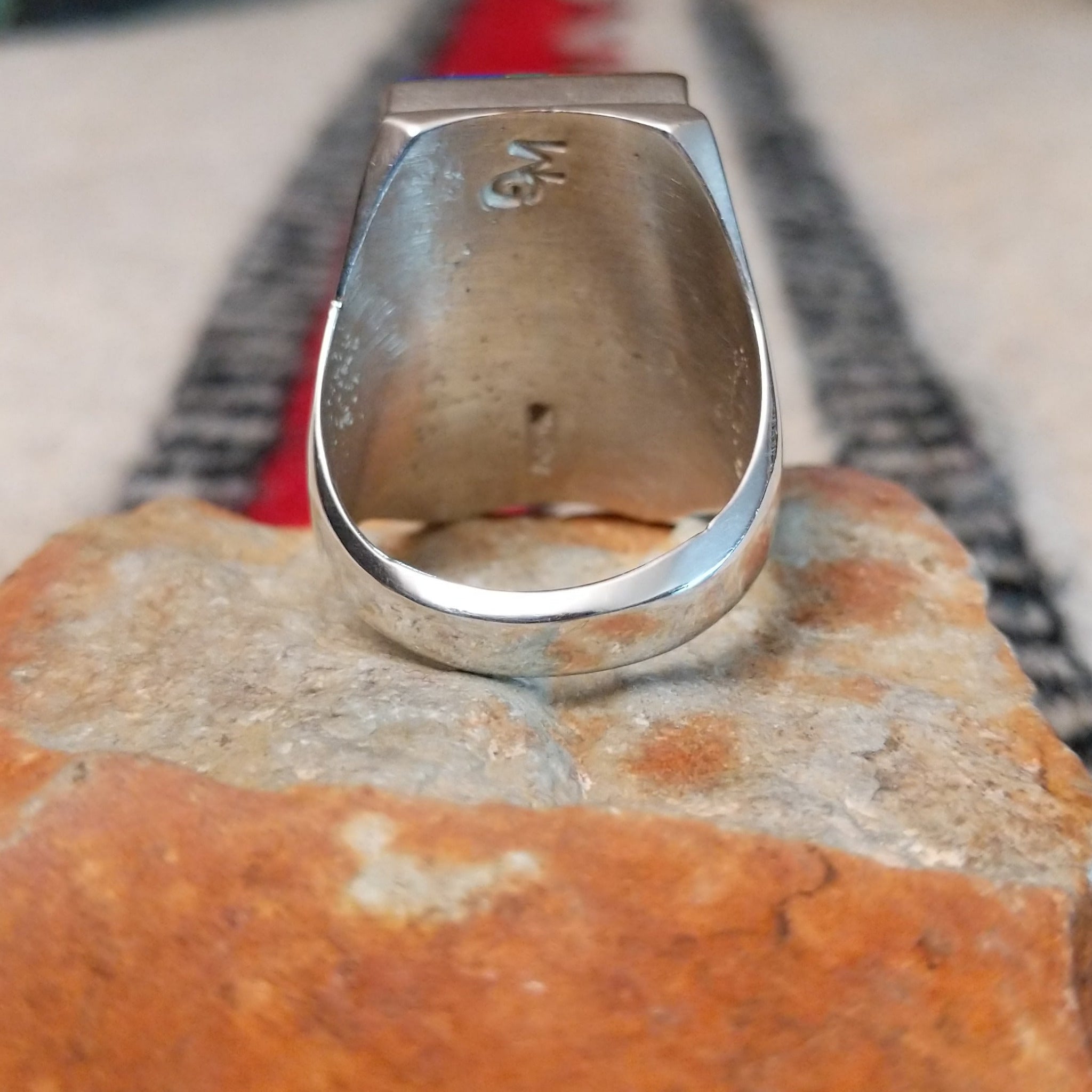 Large multistone inlay ring by Wilbert Grey featuring a rectangular geometric design of orange-red shell, turquoise, and deep blue stones with silver channel accents in a wide polished silver band; underside view.
