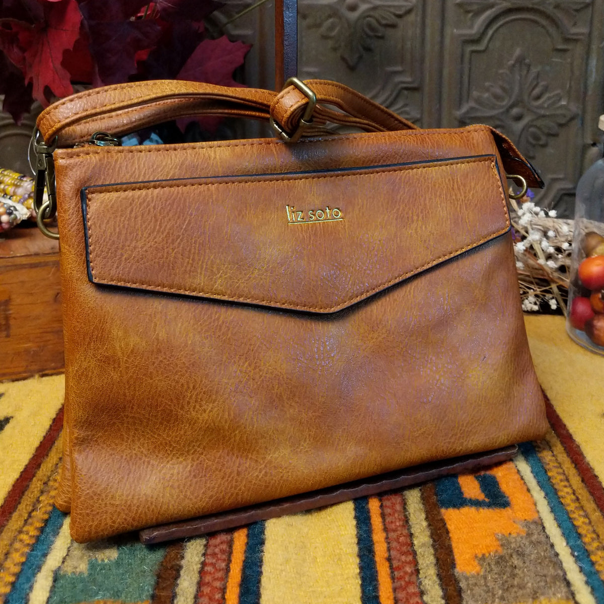 Lexi Crossbody Bag by Liz Soto featuring a streamlined silhouette, textured exterior, envelope-style front pocket, adjustable shoulder strap, metal hardware, and Liz Soto logo.