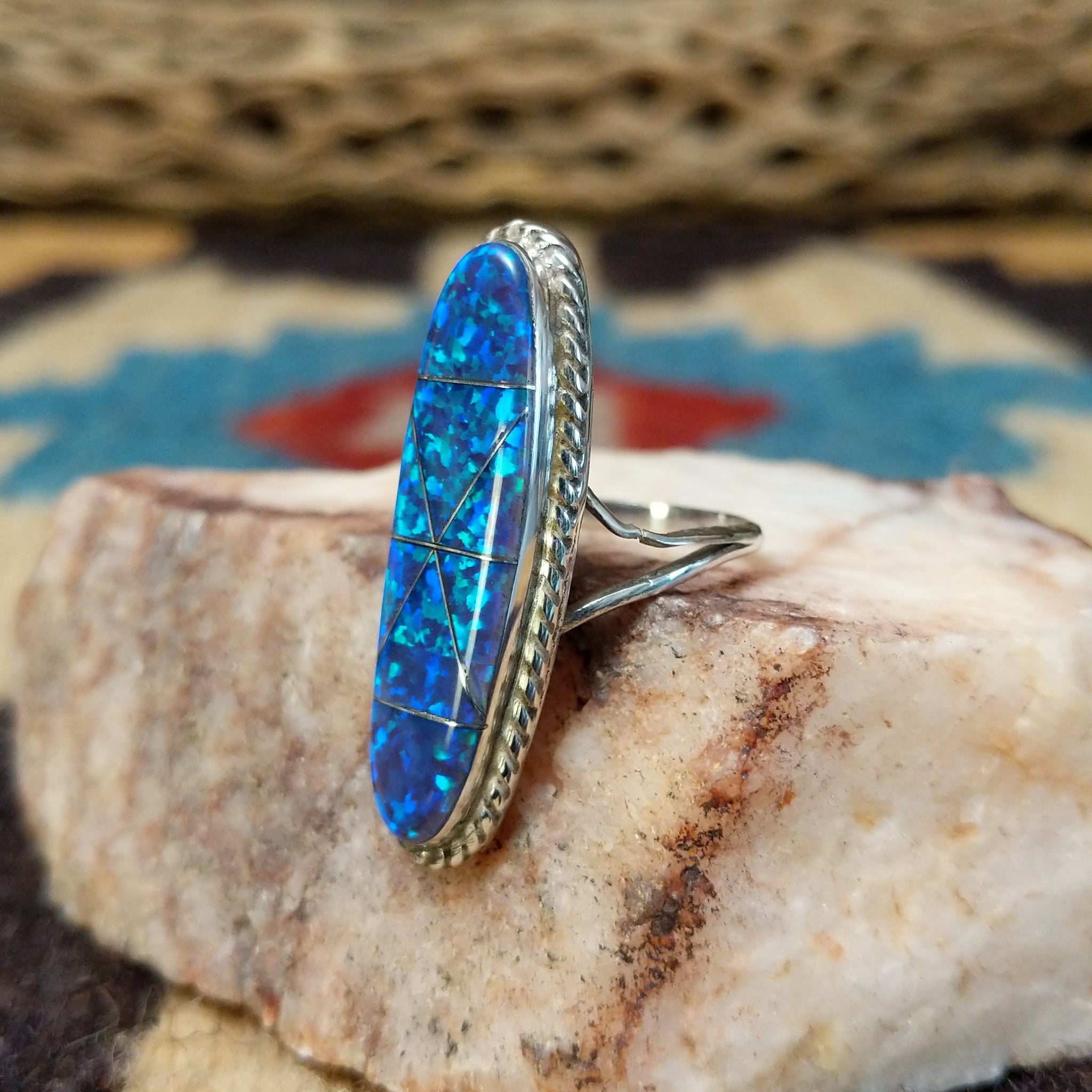 Long oval manmade opal ring by Wilbur Wauneka, featuring a shimmering oval opal with vibrant flashes of color set in a handcrafted sterling silver band. Side view.