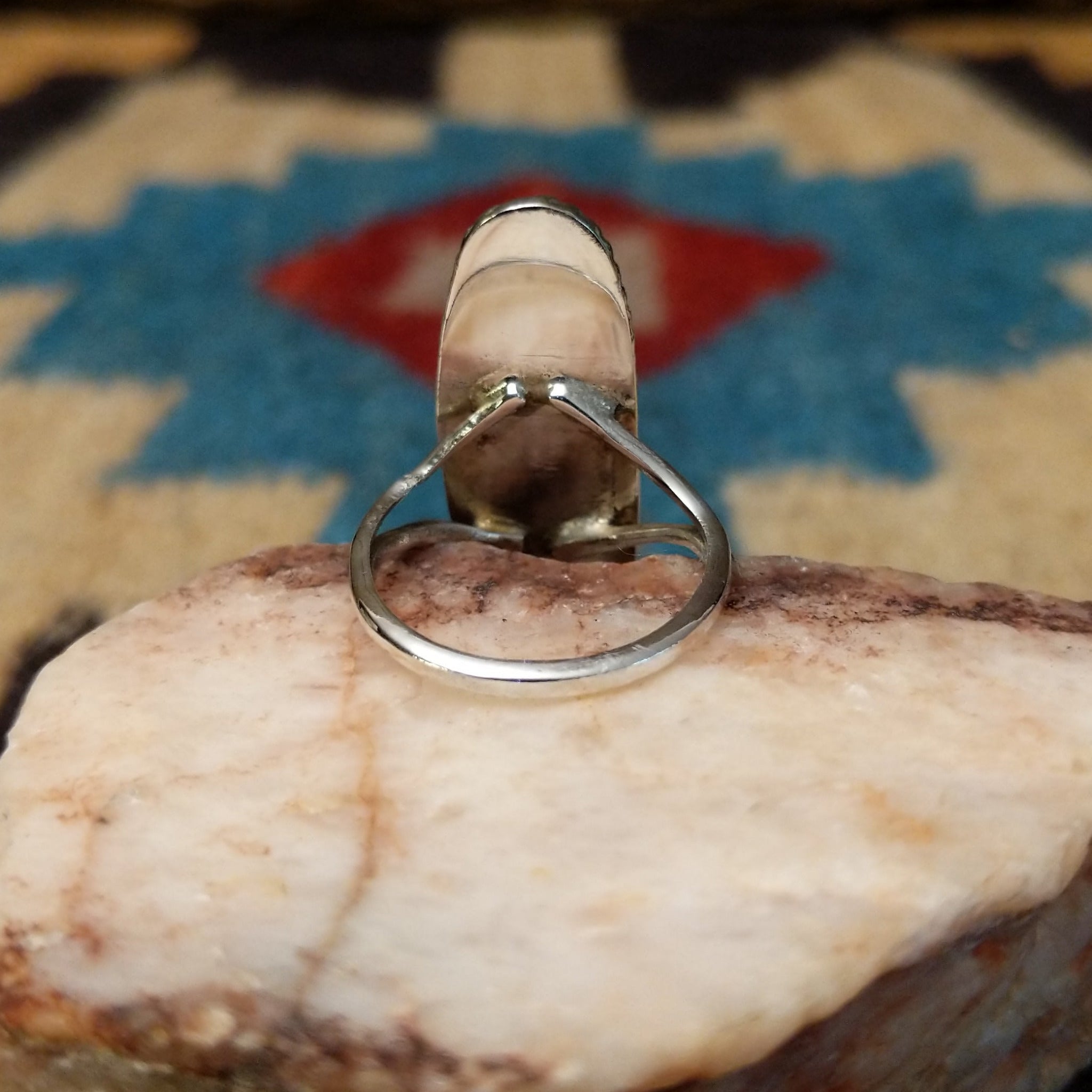 Long oval manmade opal ring by Wilbur Wauneka, featuring a shimmering oval opal with vibrant flashes of color set in a handcrafted sterling silver band. Underside view.