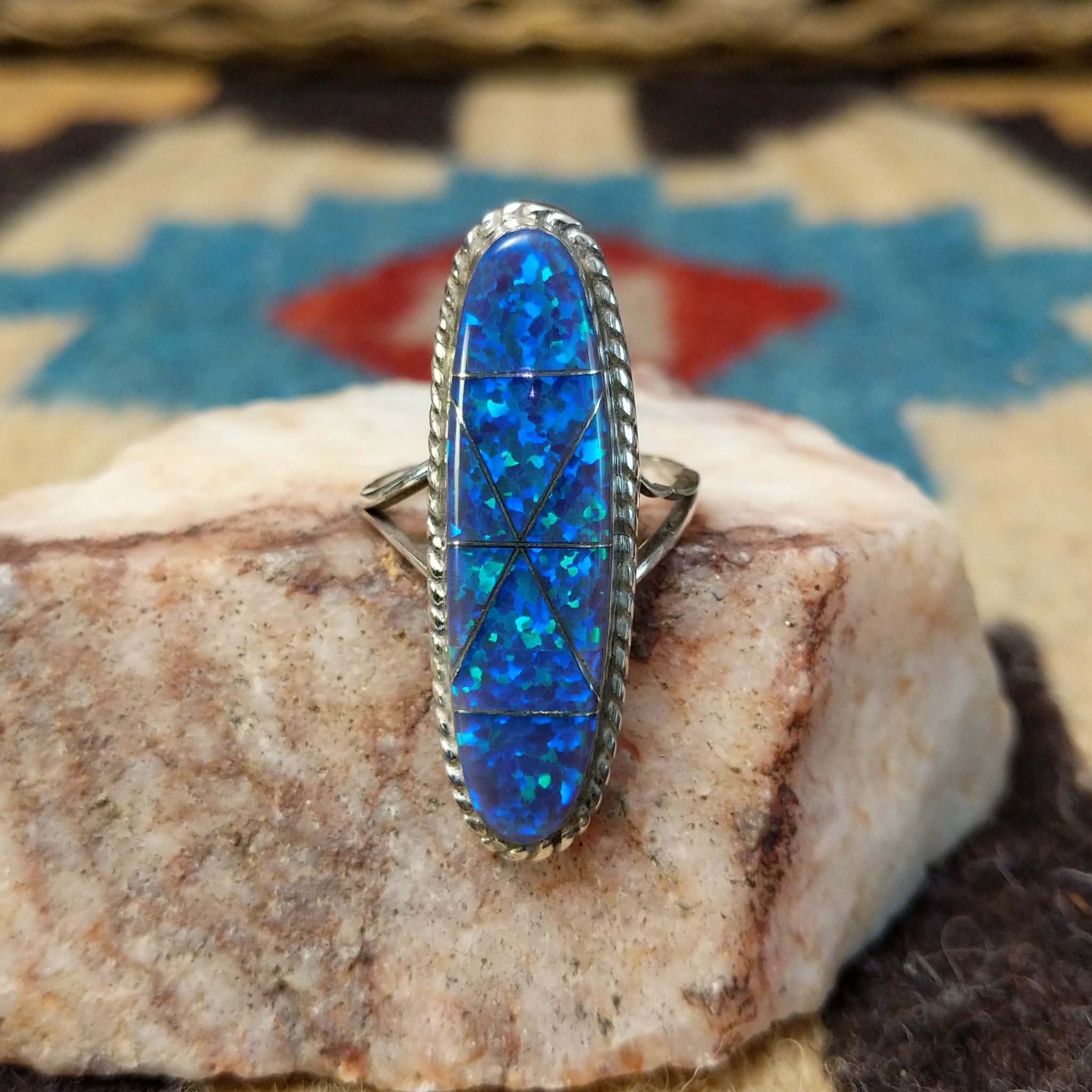 Long oval manmade opal ring by Wilbur Wauneka, featuring a shimmering oval opal with vibrant flashes of color set in a handcrafted sterling silver band.