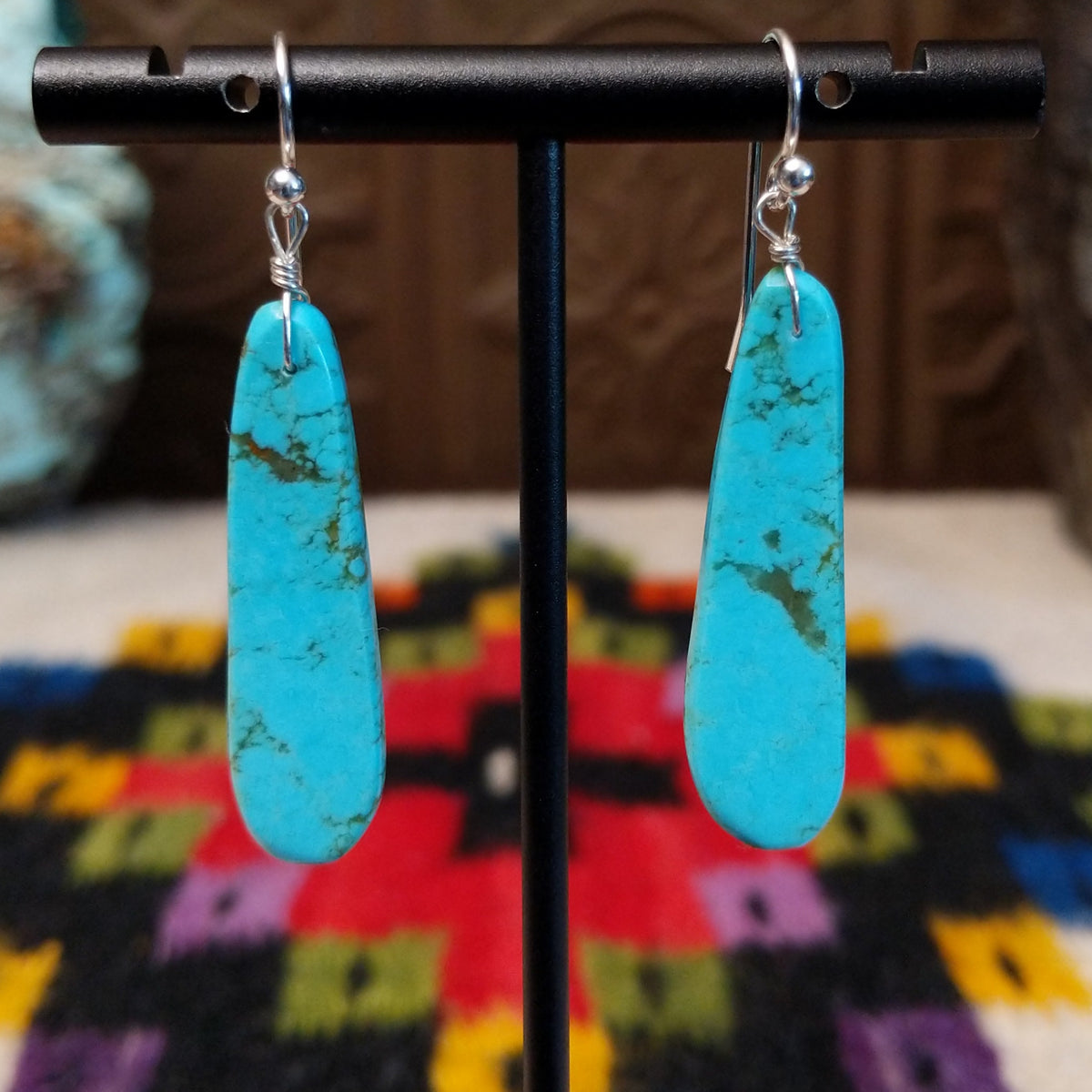 Long Slab Turquoise Earrings by Ronald Chavez featuring elongated bright blue turquoise stones with natural brown and green matrix, suspended from silver hooks.