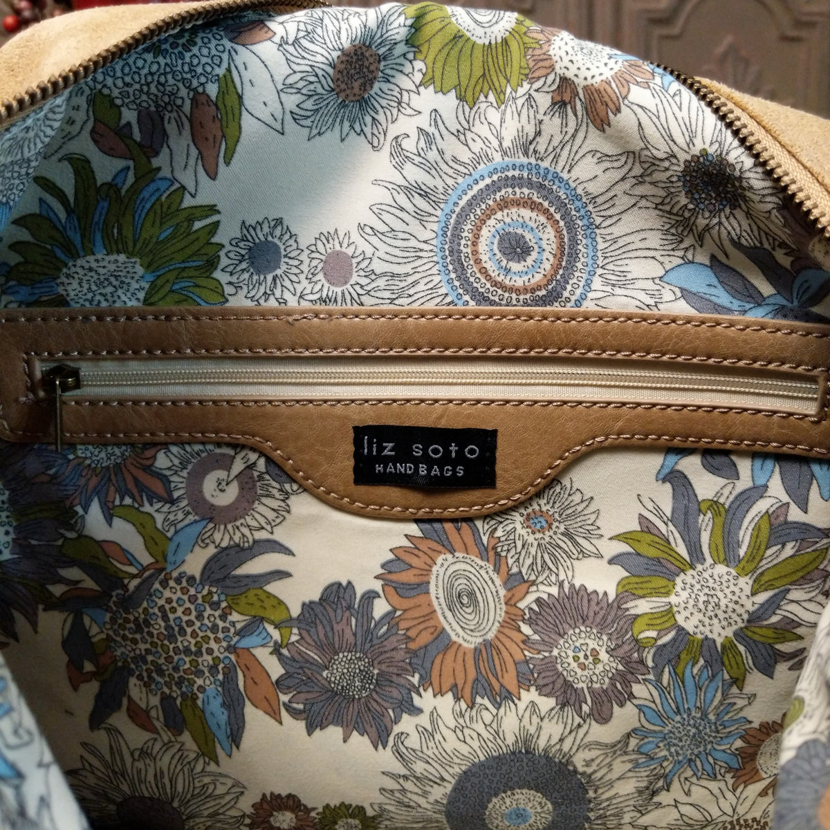 Lulu Handbag by Liz Soto featuring a spacious hobo silhouette, soft suede-like exterior, long shoulder strap, side buckle detailing, top zip closure, and logo plaque; interior zipper.
