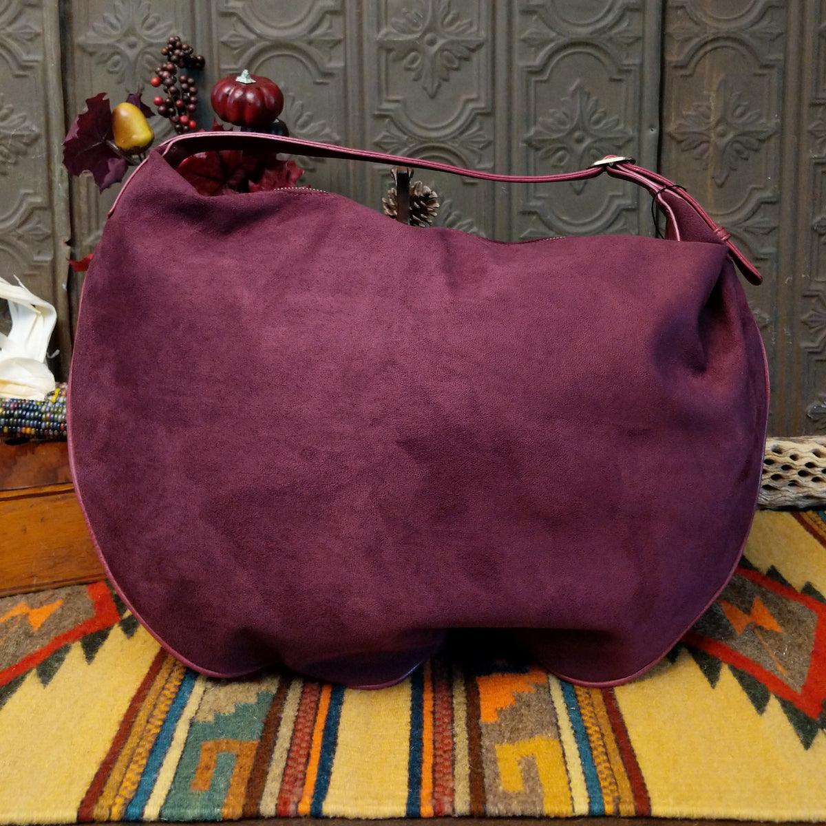 Lulu Handbag by Liz Soto featuring a spacious hobo silhouette, soft suede-like exterior, long shoulder strap, side buckle detailing, top zip closure, and logo plaque; back.