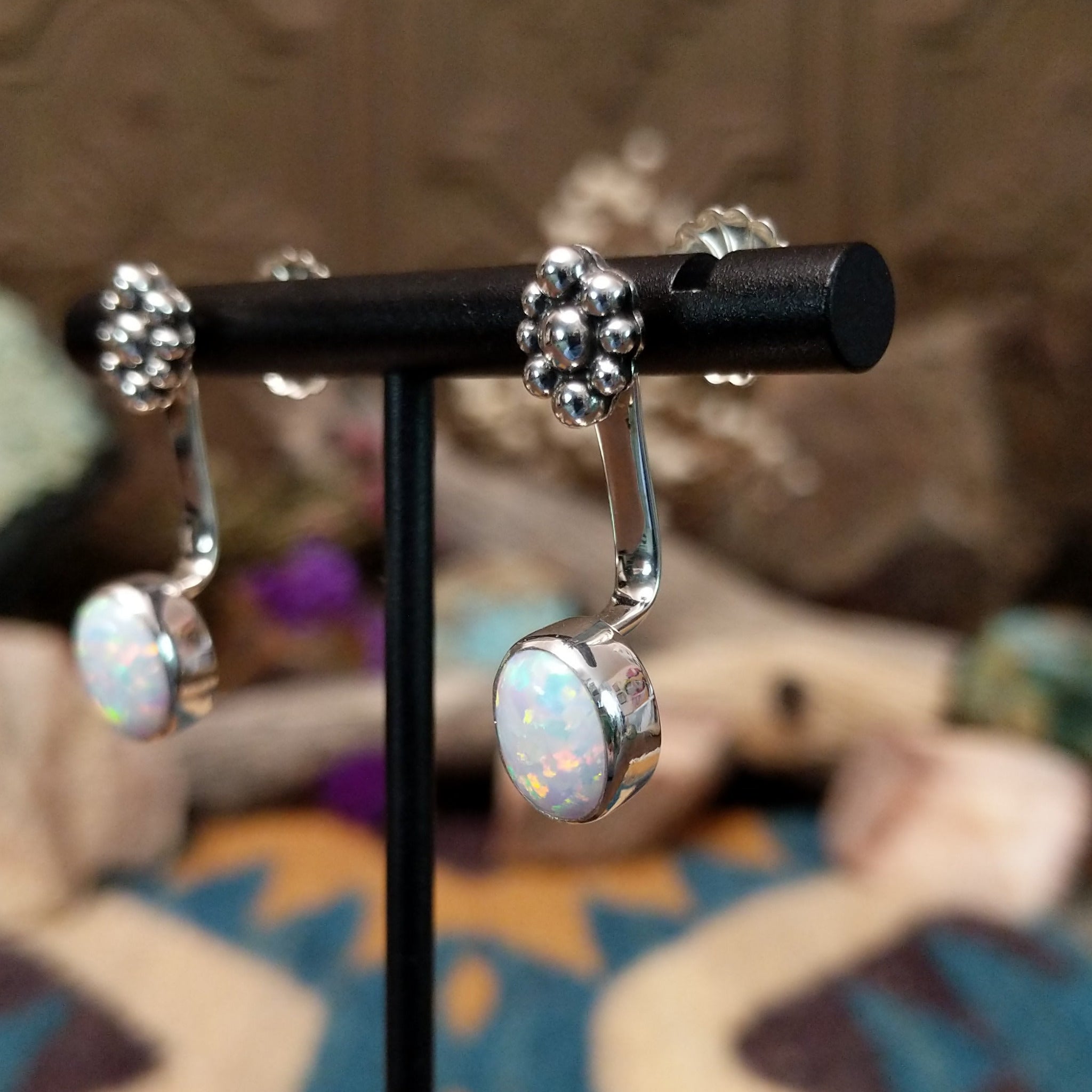 Handcrafted sterling silver adjustable earrings by Terry Wood featuring oval manmade opal cabochons with colorful iridescence and traditional Navajo silver bead cluster accents; side view.