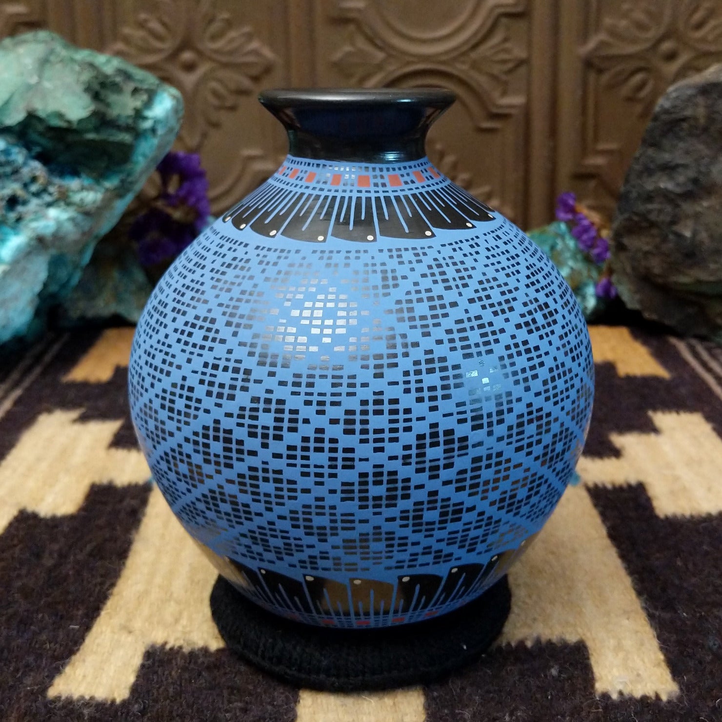 Blue Mata Ortiz pottery vase with a flared black neck, featuring intricate geometric patterns of small black squares and red accent details near the rim.