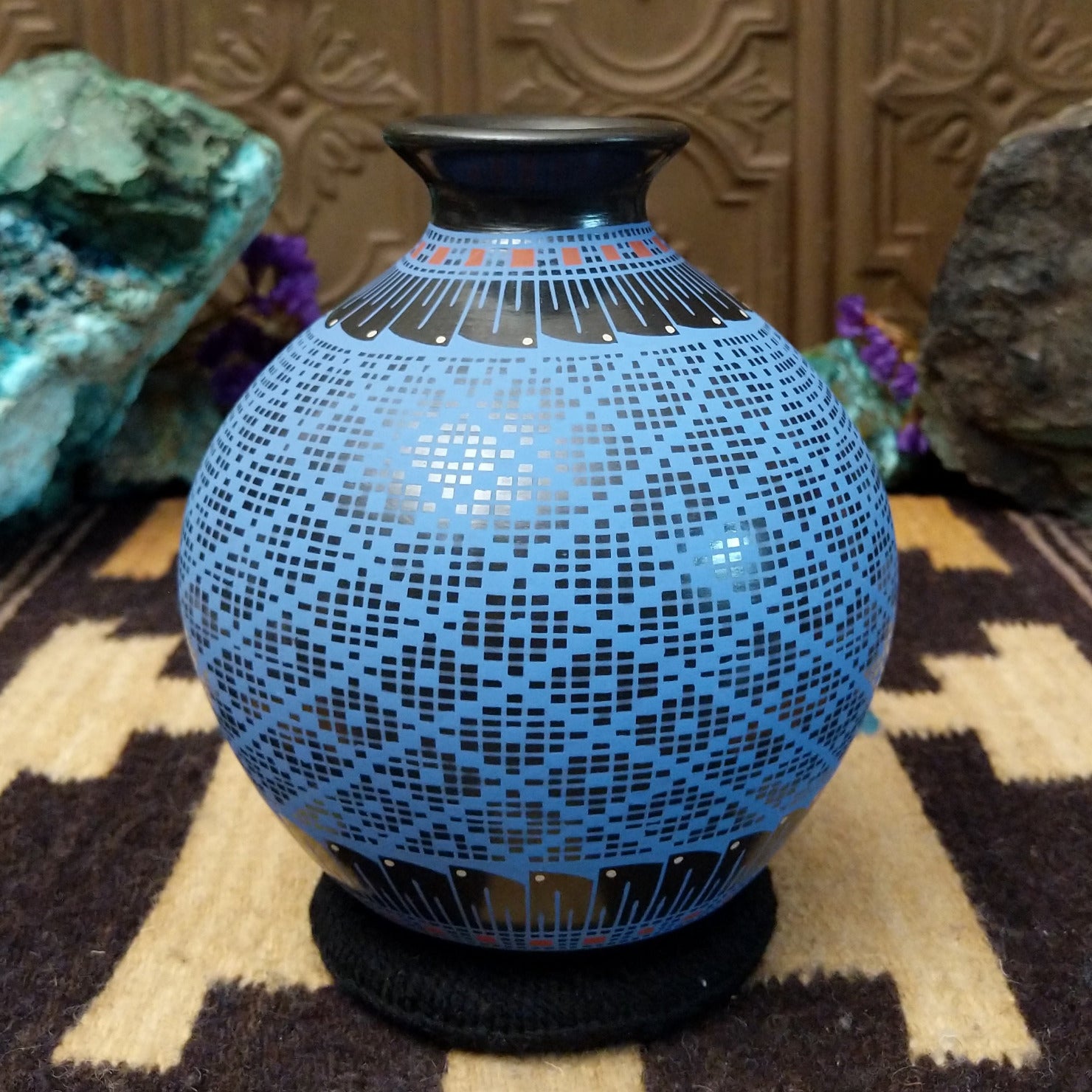 Blue Mata Ortiz pottery vase with a flared black neck, featuring intricate geometric patterns of small black squares and red accent details near the rim.
