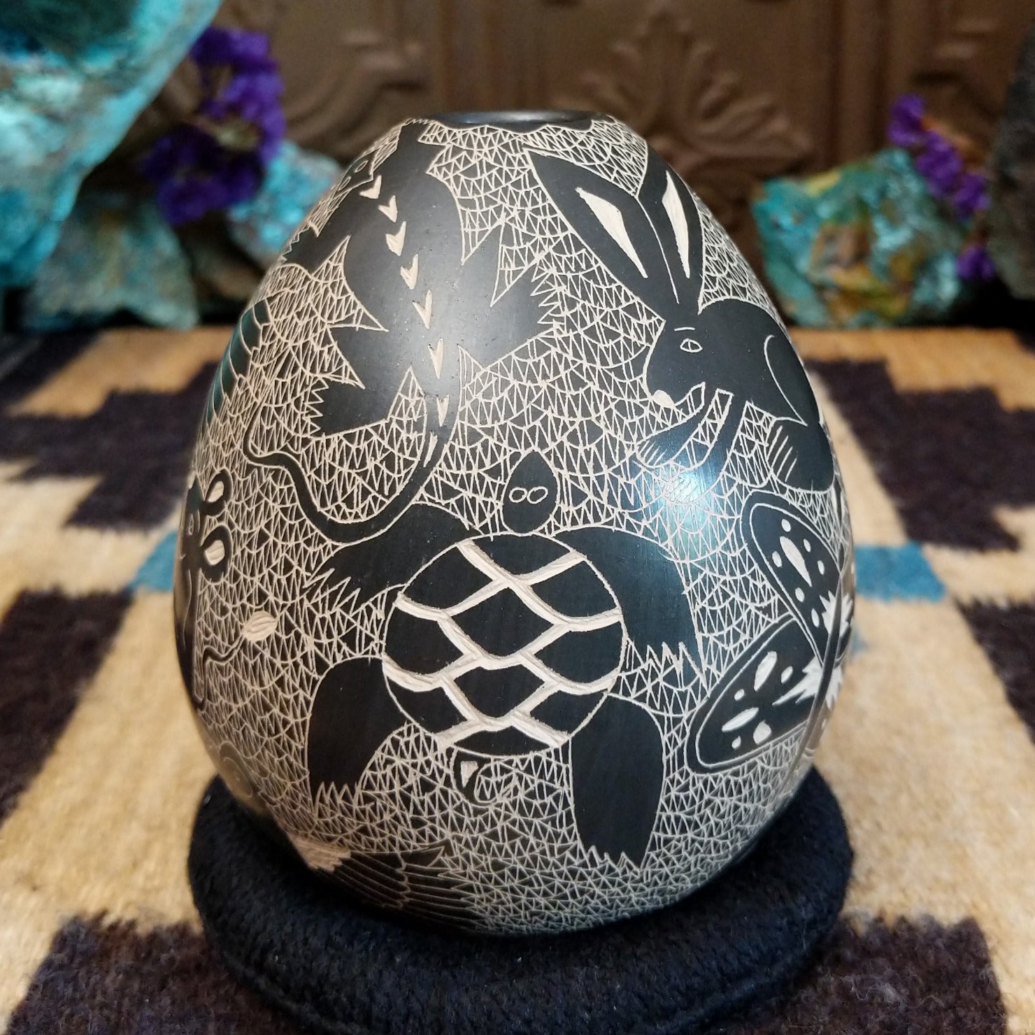 Egg-shaped Mata Ortiz pottery vessel with an etched black and white wildlife design featuring multiple stylized animals.