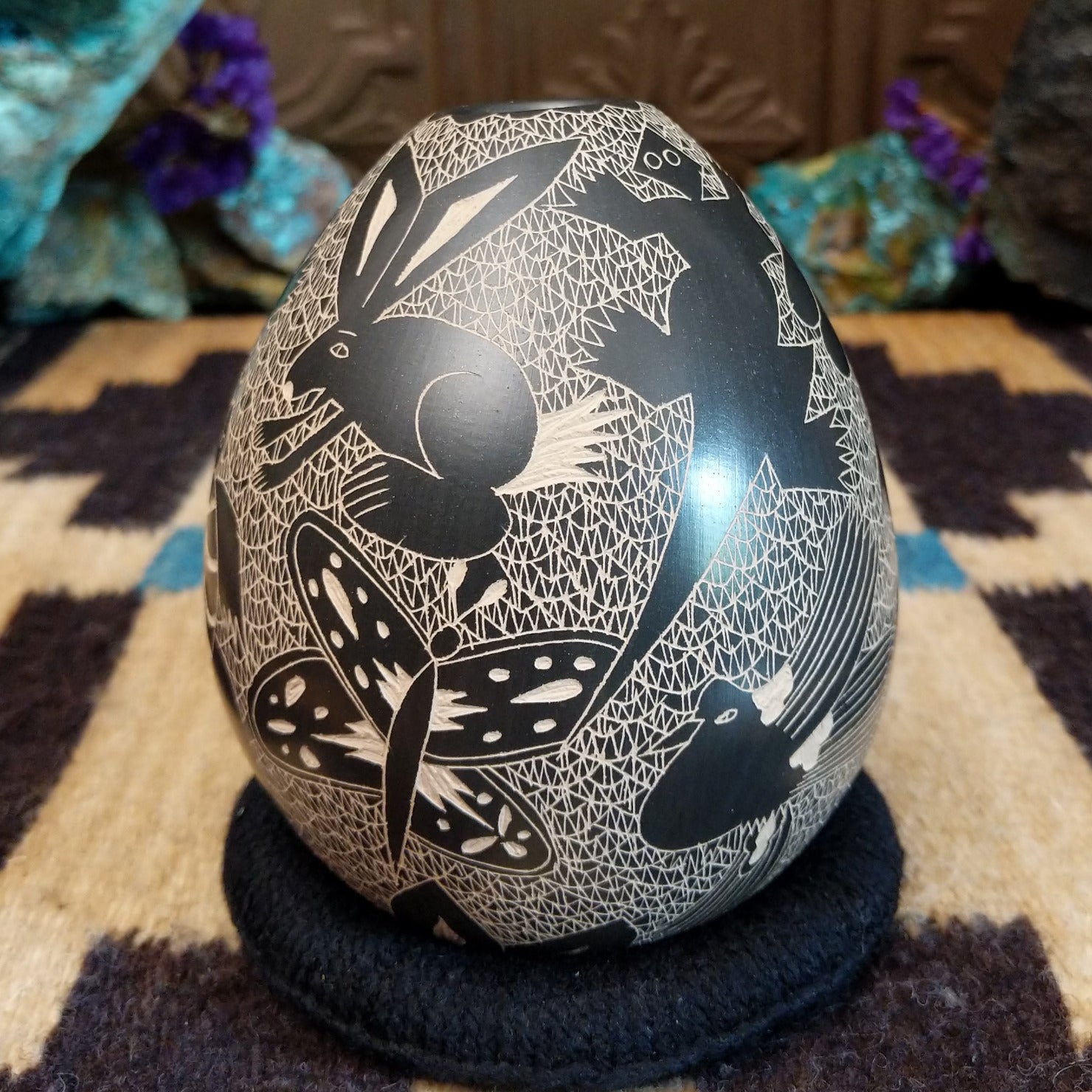 Egg-shaped Mata Ortiz pottery vessel with an etched black and white wildlife design featuring multiple stylized animals.