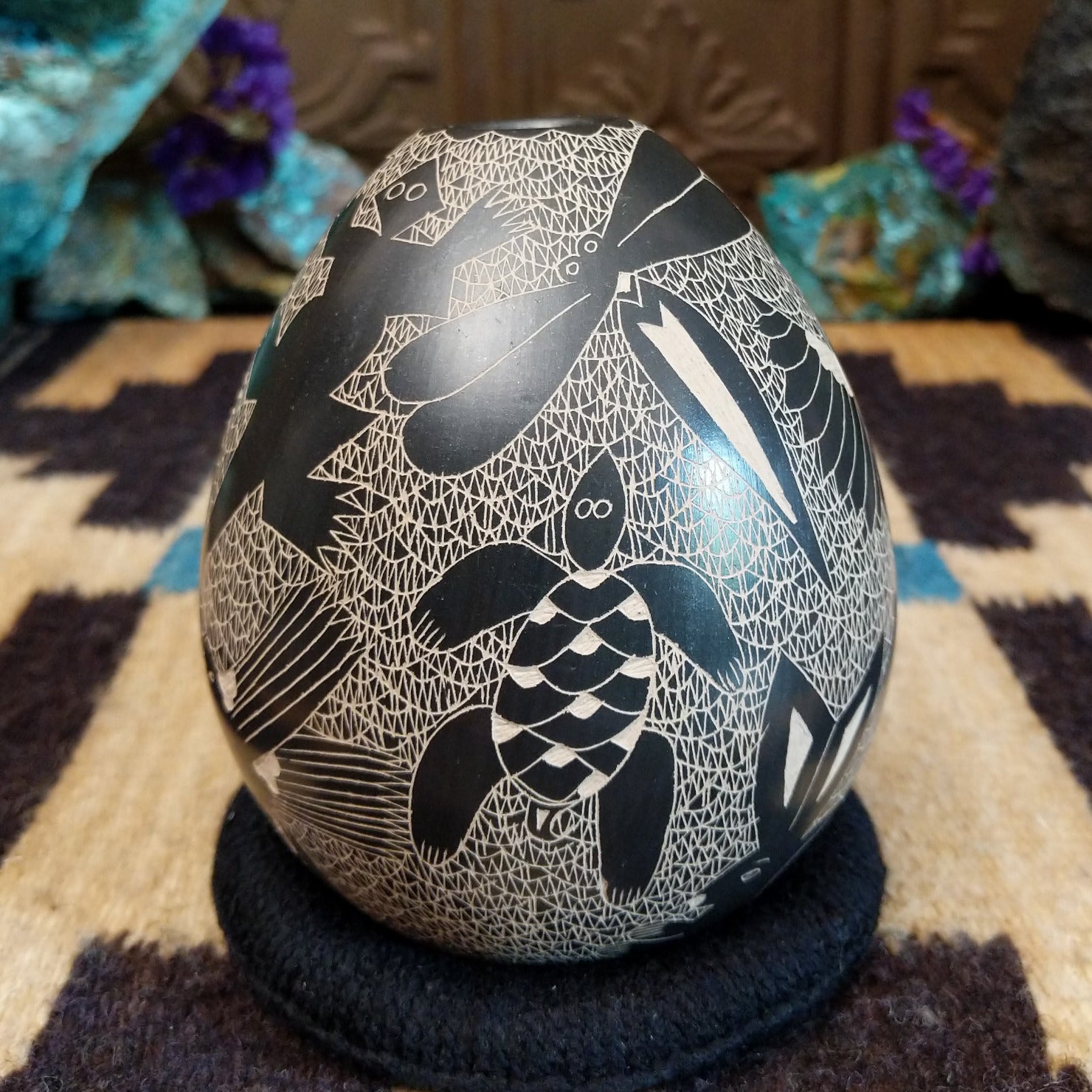 Egg-shaped Mata Ortiz pottery vessel with an etched black and white wildlife design featuring multiple stylized animals.