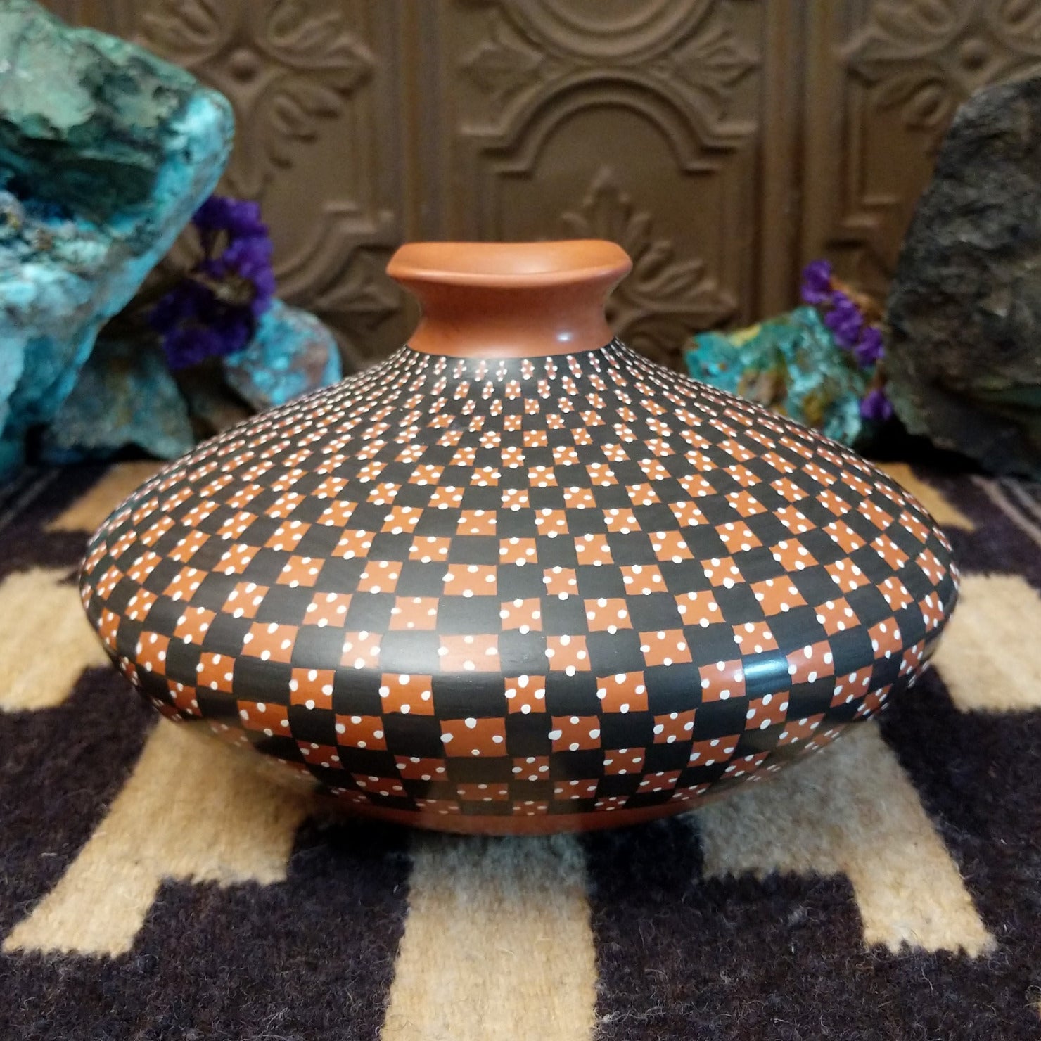 Low-profile Mata Ortiz pottery jar with a geometric checkerboard pattern in black and clay tones, featuring white dotted accents and a squared neck opening.