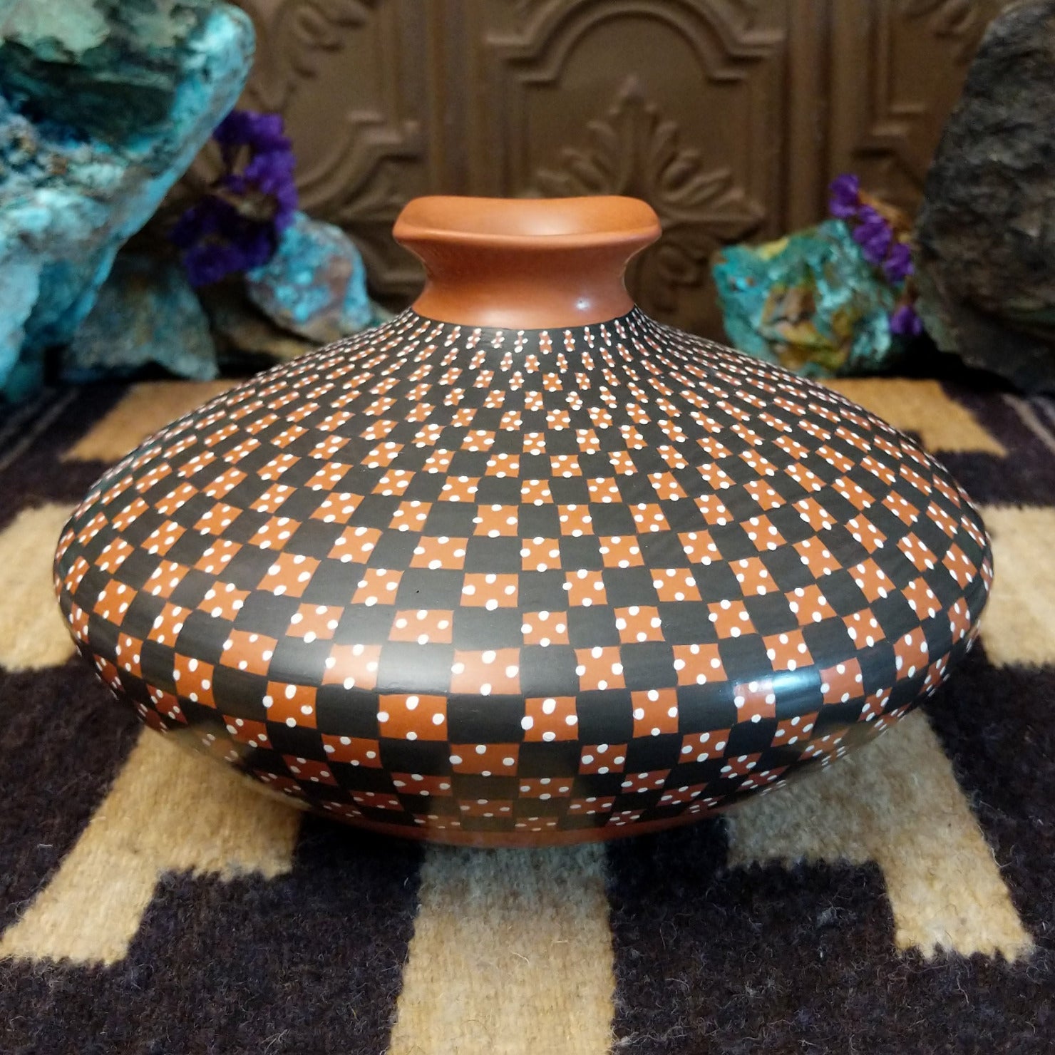 Low-profile Mata Ortiz pottery jar with a geometric checkerboard pattern in black and clay tones, featuring white dotted accents and a squared neck opening.