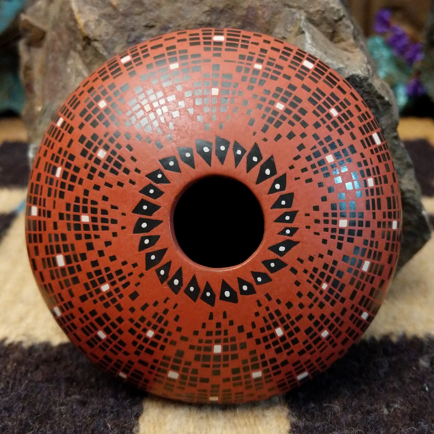 Rounded Mata Ortiz seed pot with a red clay finish, featuring a radiating geometric mosaic pattern of black and white squares and a black decorative band near the base.