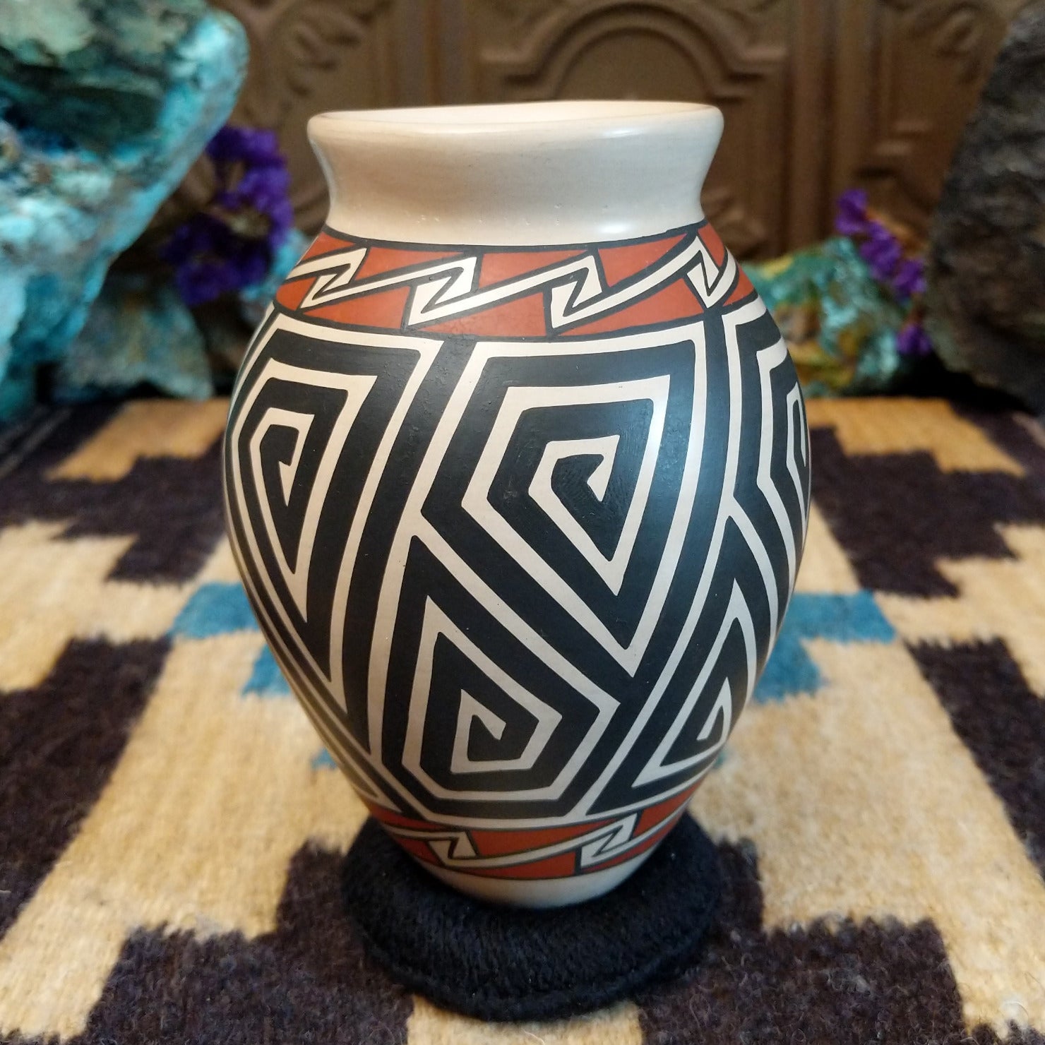 Mata Ortiz pottery vase with a cream rim, featuring bold black and cream triangle spiral patterns with warm clay accents near the neck.