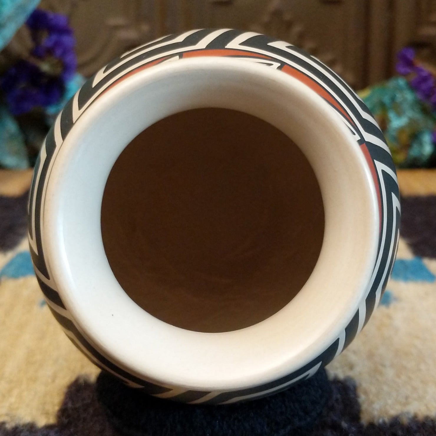 Mata Ortiz pottery vase with a cream rim, featuring bold black and cream triangle spiral patterns with warm clay accents near the neck.