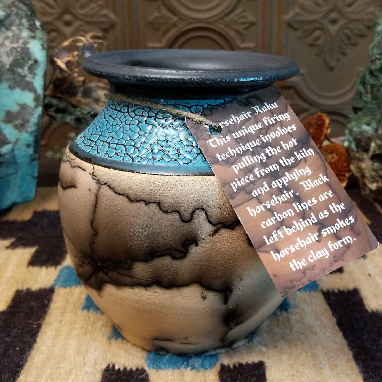 Ceramic pottery piece with horsehair fired onto the face and crackled, blue glazed top-half.