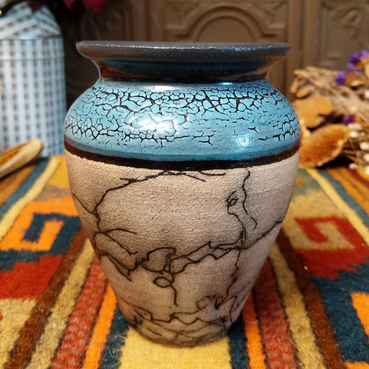 Mini horsehair pottery vase by Roger Calhoun with a flared dark rim, crackled turquoise-blue shoulder, and black horsehair markings concentrated near the base of its cream-colored body.