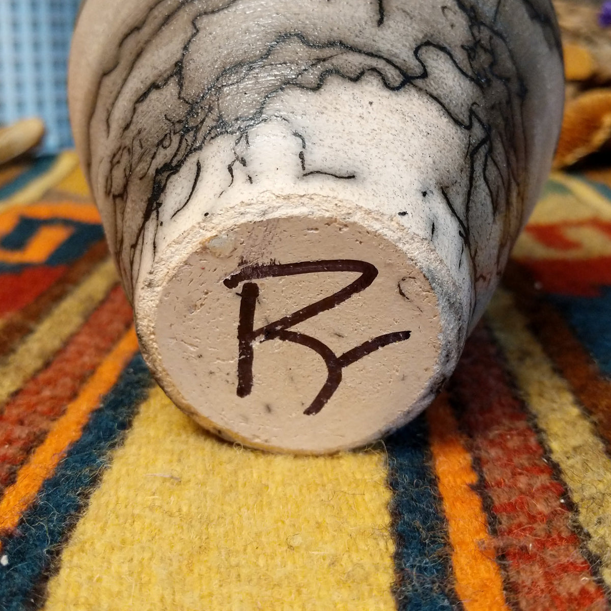 Close-up of the underside of Roger Calhoun's horsehair pottery, showing the artist's hand-painted initials on the unglazed base.