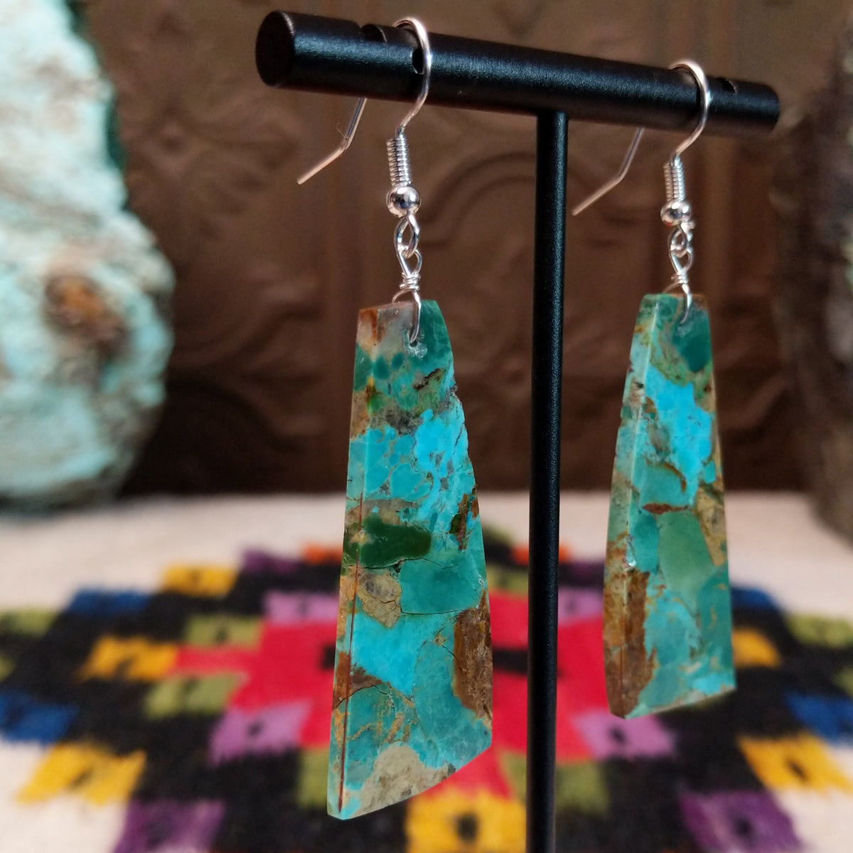 Mohave Turquoise Slab Earrings by Jameson Pete featuring elongated geometric turquoise stones with blue, green, tan, and brown matrix, suspended from silver hooks; side view.