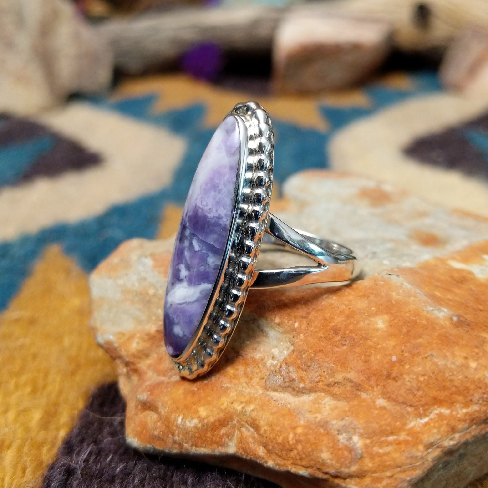 Handcrafted sterling silver ring featuring an elongated marquise-shaped Morado Opal cabochon with swirling shades of lavender, deep purple, and creamy white, set in a polished sterling silver beaded bezel; side view.