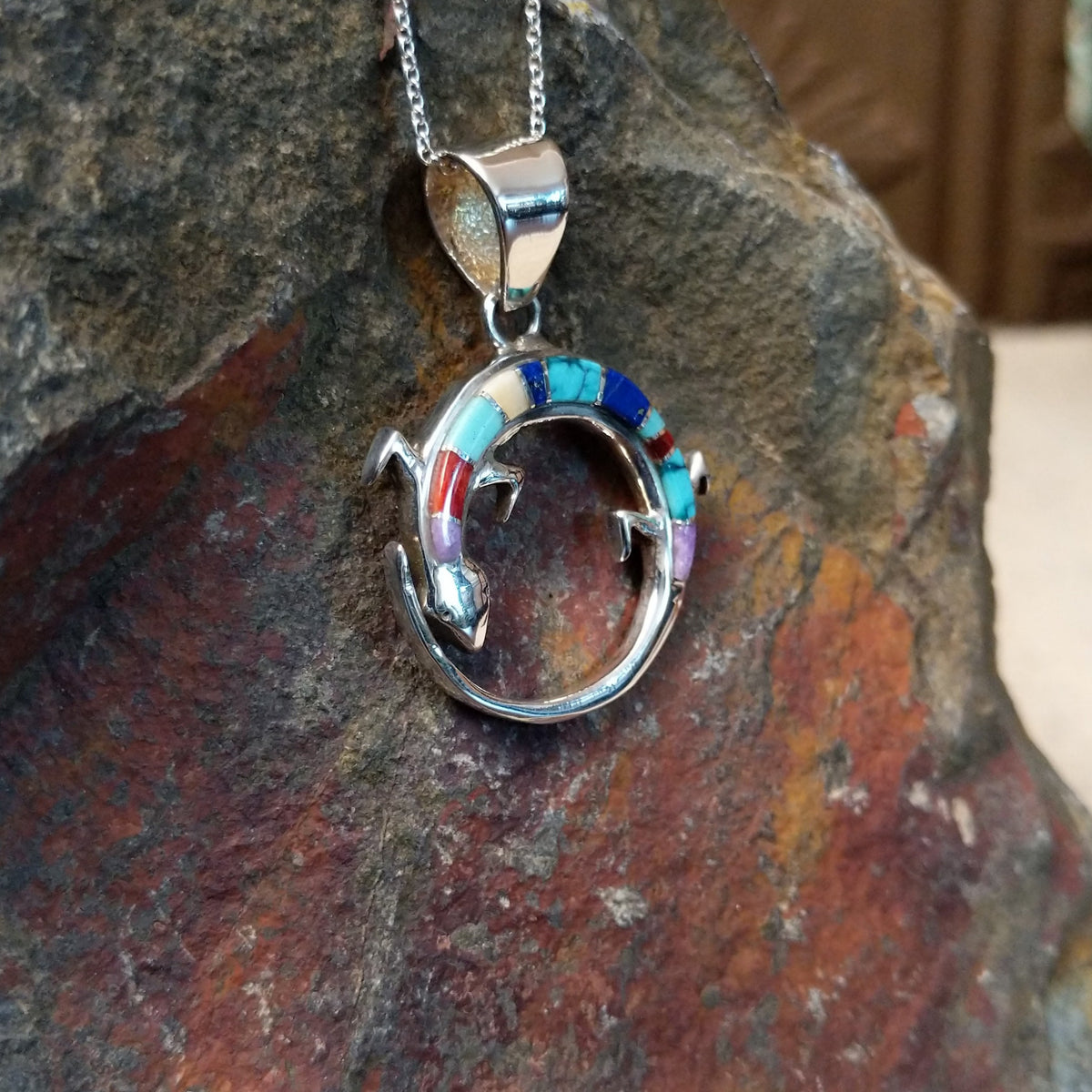 Multistone inlay lizard pendant by Ambrose Tsosie featuring a circular sterling silver lizard design accented with turquoise, blue, red, purple, and cream-colored stone inlay; side view.