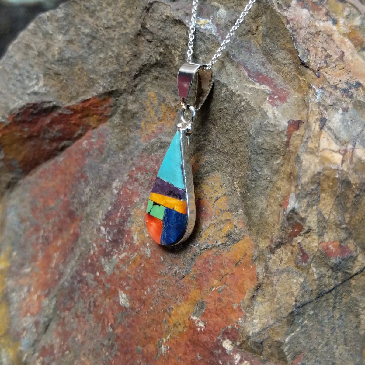 Multistone inlay teardrop pendant by P. Smith featuring turquoise, purple, orange, green, red, and blue stones arranged in a colorful geometric design; side view.