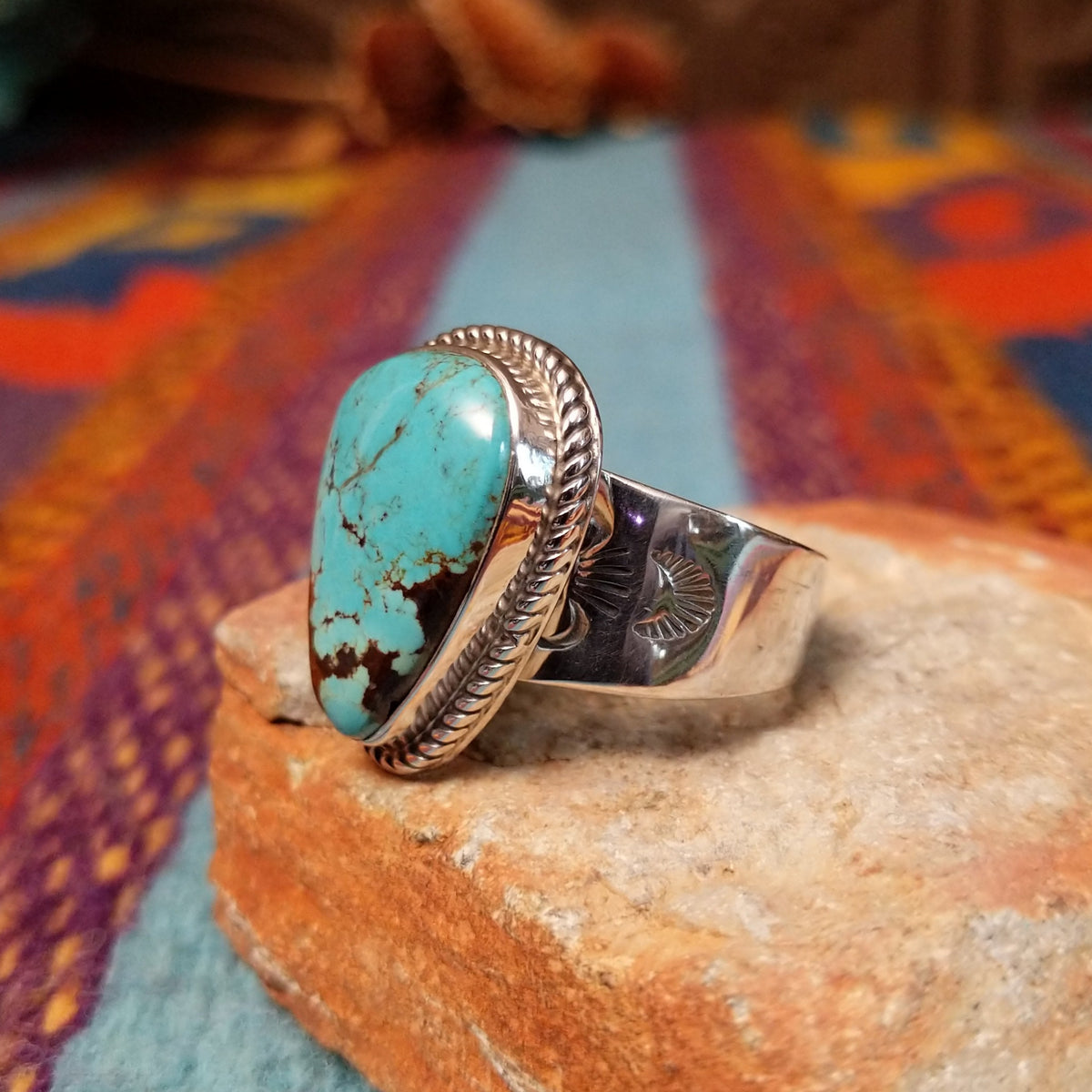 Navajo #8 Turquoise Ring featuring a large freeform blue turquoise cabochon with prominent brown matrix, framed by twisted silver rope detailing in a polished silver setting; side view.