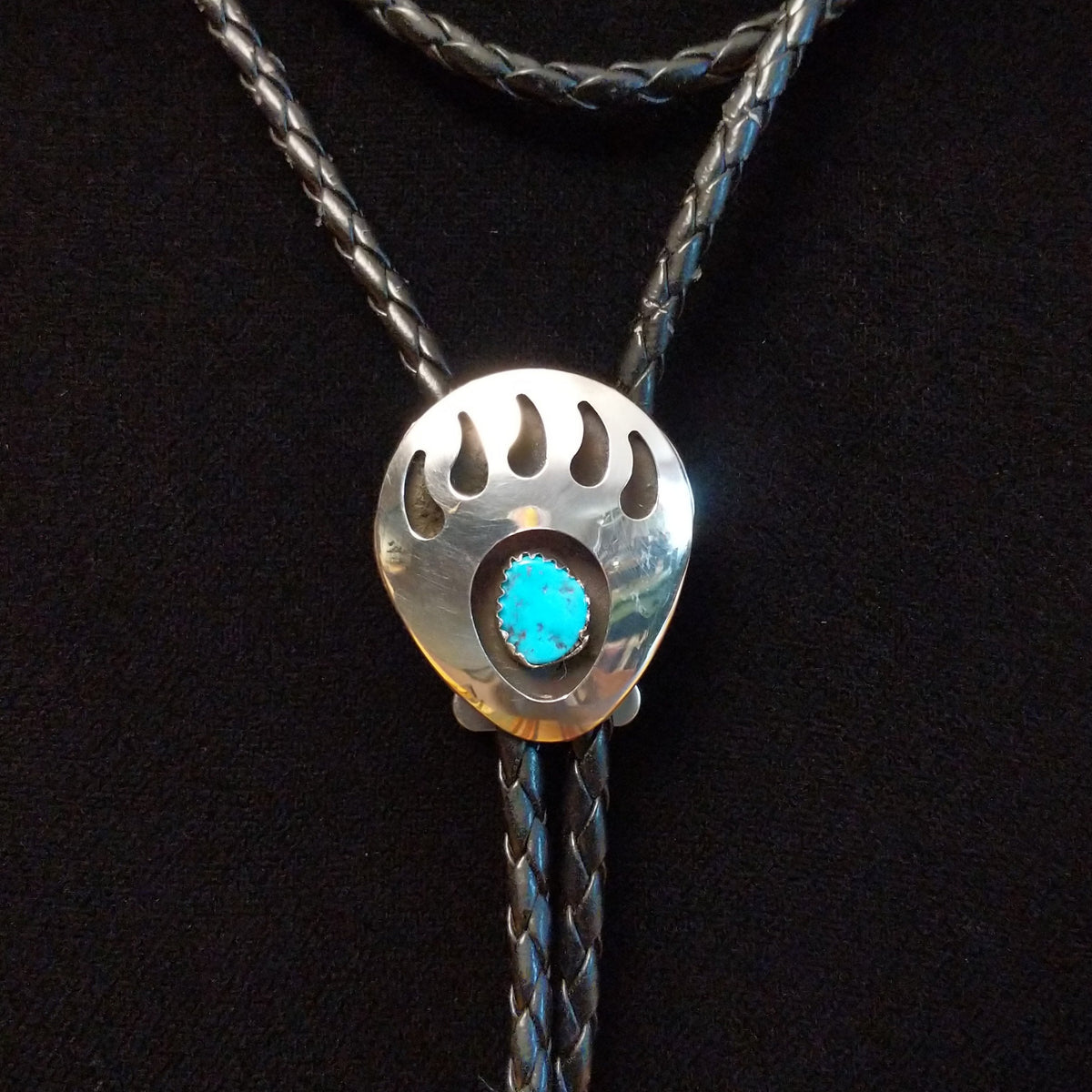 A sterling silver bolo tie necklace featuring a paw print design with a turquoise stone inlay, displayed on a black background.