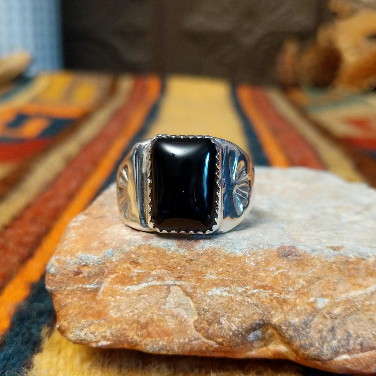 Navajo Black Onyx Ring featuring a polished rectangular black onyx gemstone in a sawtooth silver bezel, with a wide silver band accented by stamped fan-shaped designs on both sides.