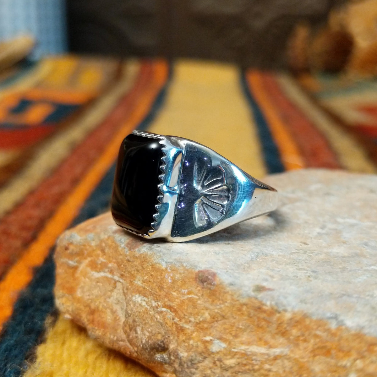 Navajo Black Onyx Ring featuring a polished rectangular black onyx gemstone in a sawtooth silver bezel, with a wide silver band accented by stamped fan-shaped designs on both sides; side view.