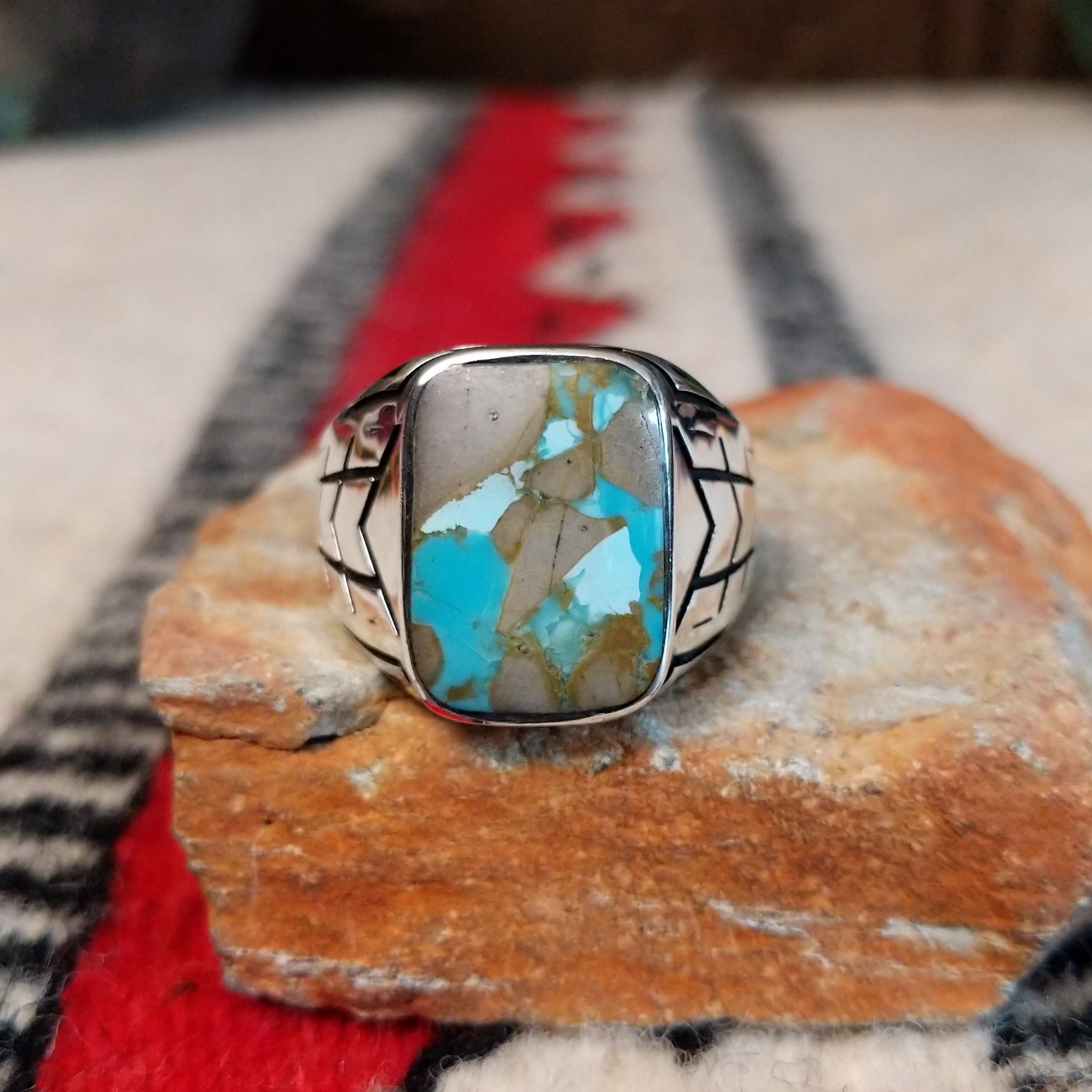 Navajo Boulder Turquoise Ring by E. featuring a rectangular turquoise stone with prominent natural brown host rock, set in a polished silver band with geometric stamped accents.