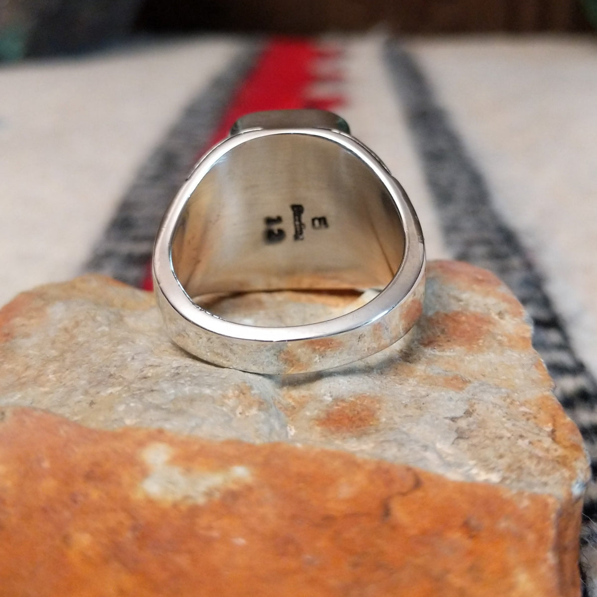 Navajo Boulder Turquoise Ring by E. featuring a rectangular turquoise stone with prominent natural brown host rock, set in a polished silver band with geometric stamped accents; underside view.