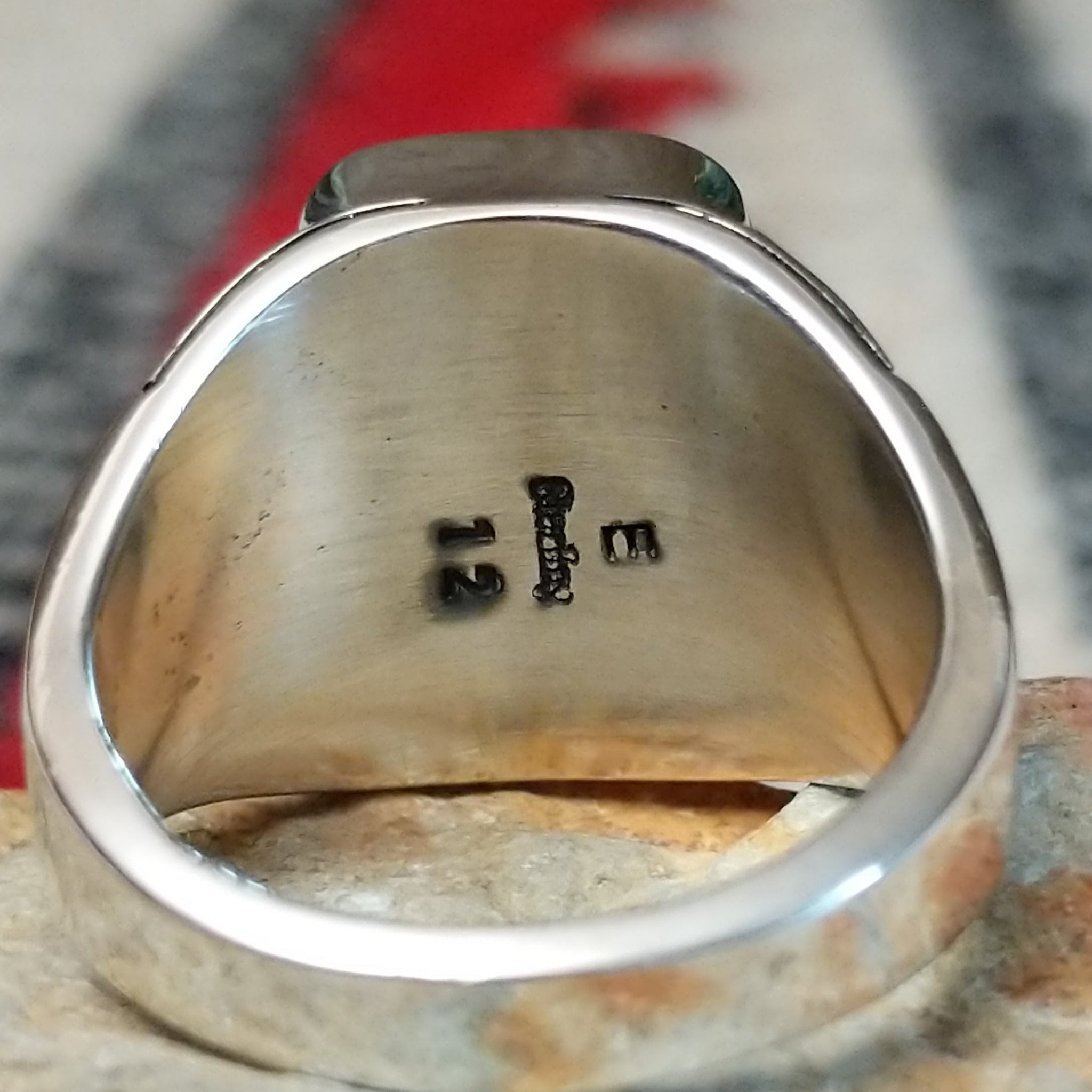 Navajo Boulder Turquoise Ring by E. featuring a rectangular turquoise stone with prominent natural brown host rock, set in a polished silver band with geometric stamped accents; artisan and Sterling Silver stamp.