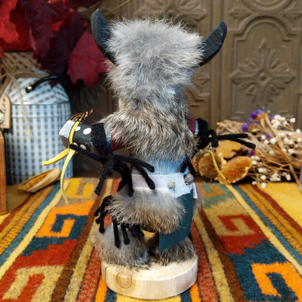 This distinctive Navajo Buffalo Kachina by Debbie James features a hand-painted wooden figure with black buffalo horns, gray fur headdress, black-and-white painted details, natural feathers, leather ties, and a wooden display base; back view.