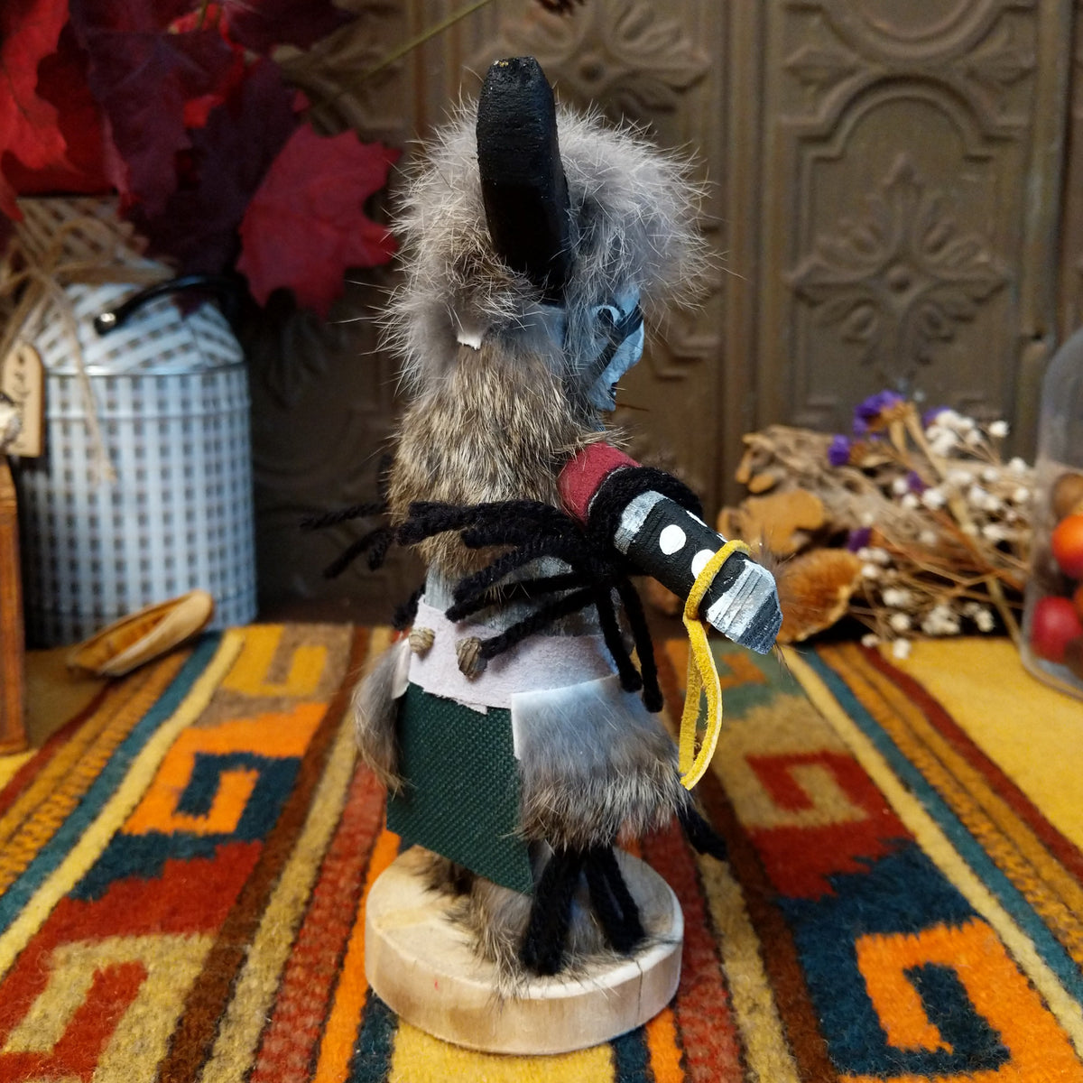 This distinctive Navajo Buffalo Kachina by Debbie James features a hand-painted wooden figure with black buffalo horns, gray fur headdress, black-and-white painted details, natural feathers, leather ties, and a wooden display base; side view.