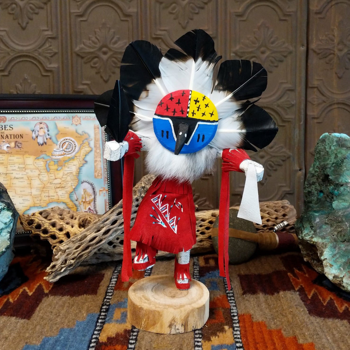 Wood carved into a chief kachina with feathers encircling its head, vibrant paint, and red suede clothing.
