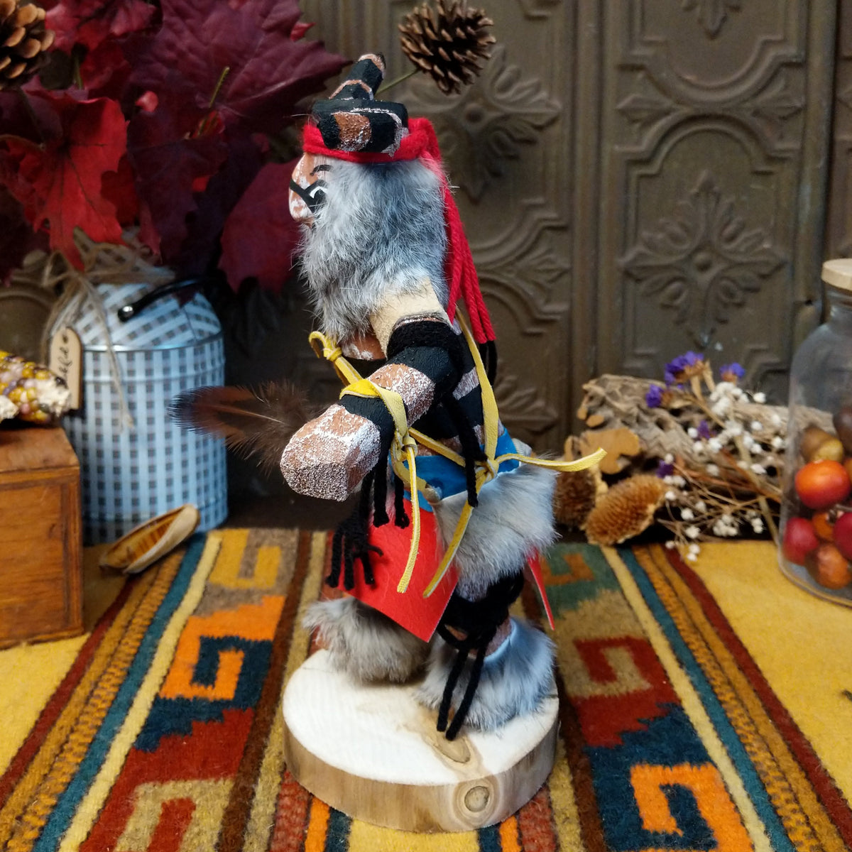 Side view of the Navajo Ogre Kachina doll with gray fur-covered face, black horns with turquoise markings, open red mouth, pointed teeth, and green fabric apron.