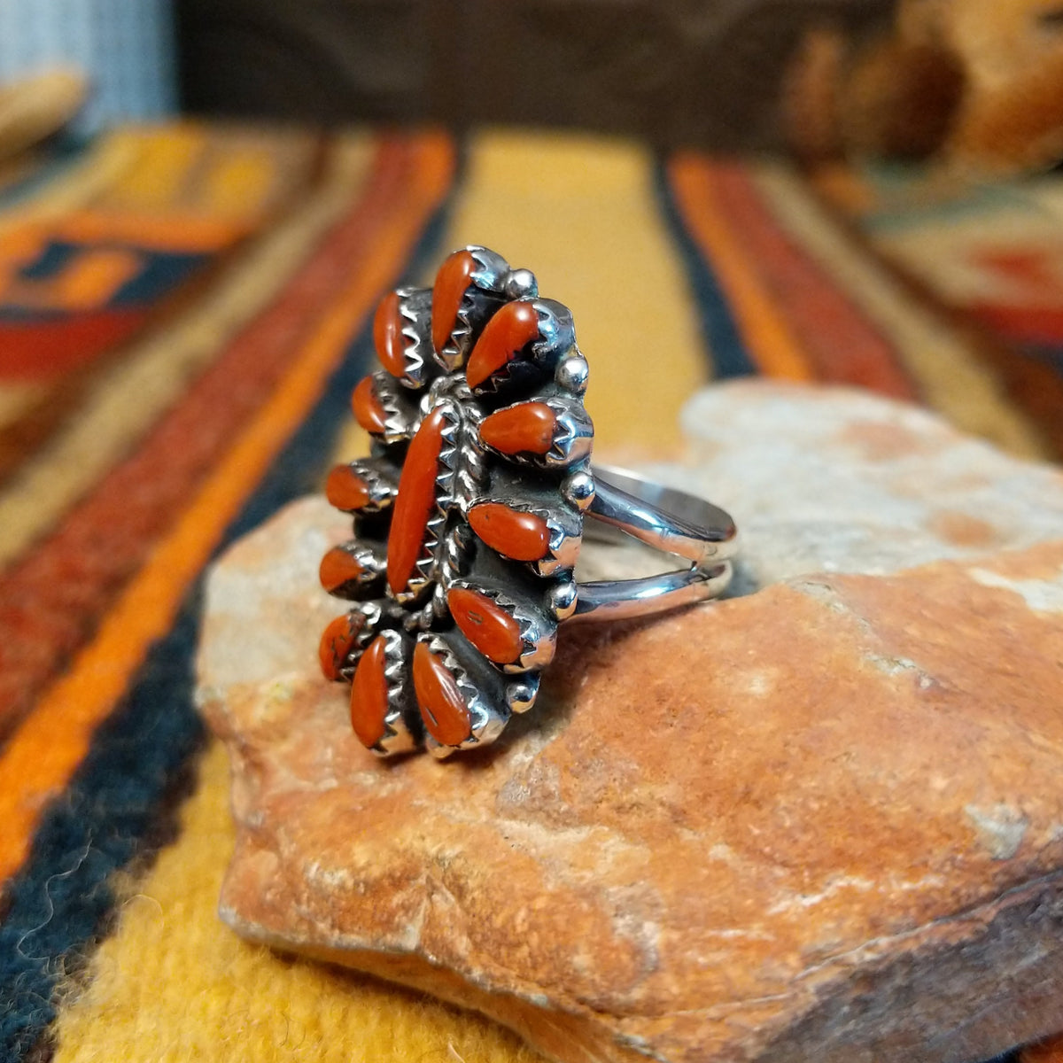 Angled side view of a sterling silver coral concho ring showing raised serrated stone settings, dimensional silverwork, and a polished split-shank band.
