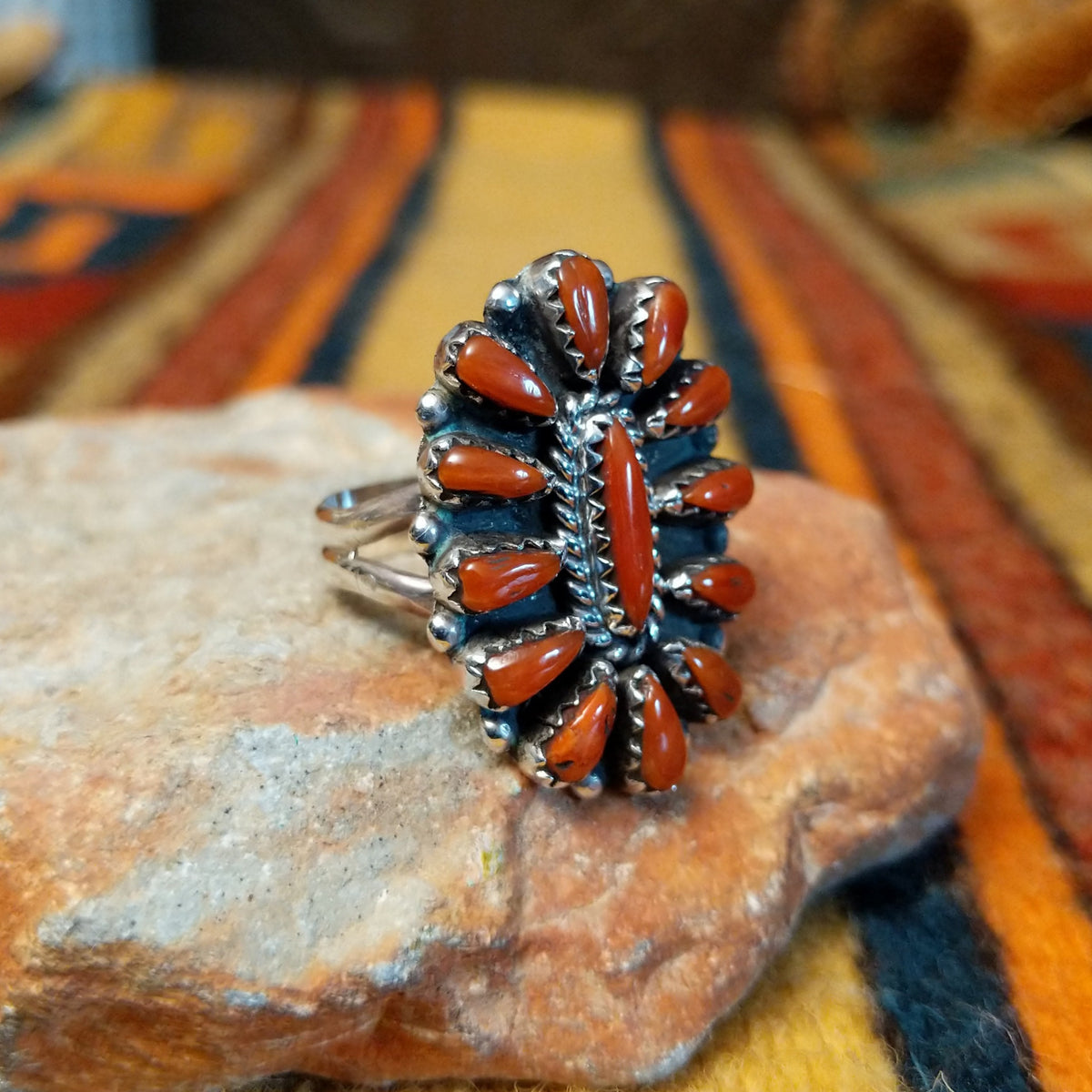 Opposite side view of a sterling silver coral concho ring showing raised serrated stone settings, dimensional silverwork, and a polished split-shank band.